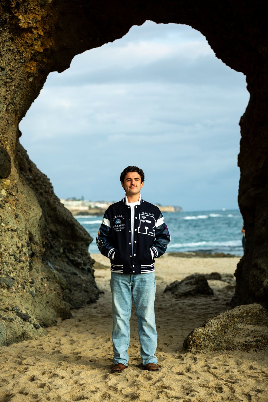 Figure stands in natural stone archway at rocky beach during cloudy day. Beach photography, Huntington Beach, Laguna Beach, Redlands photog