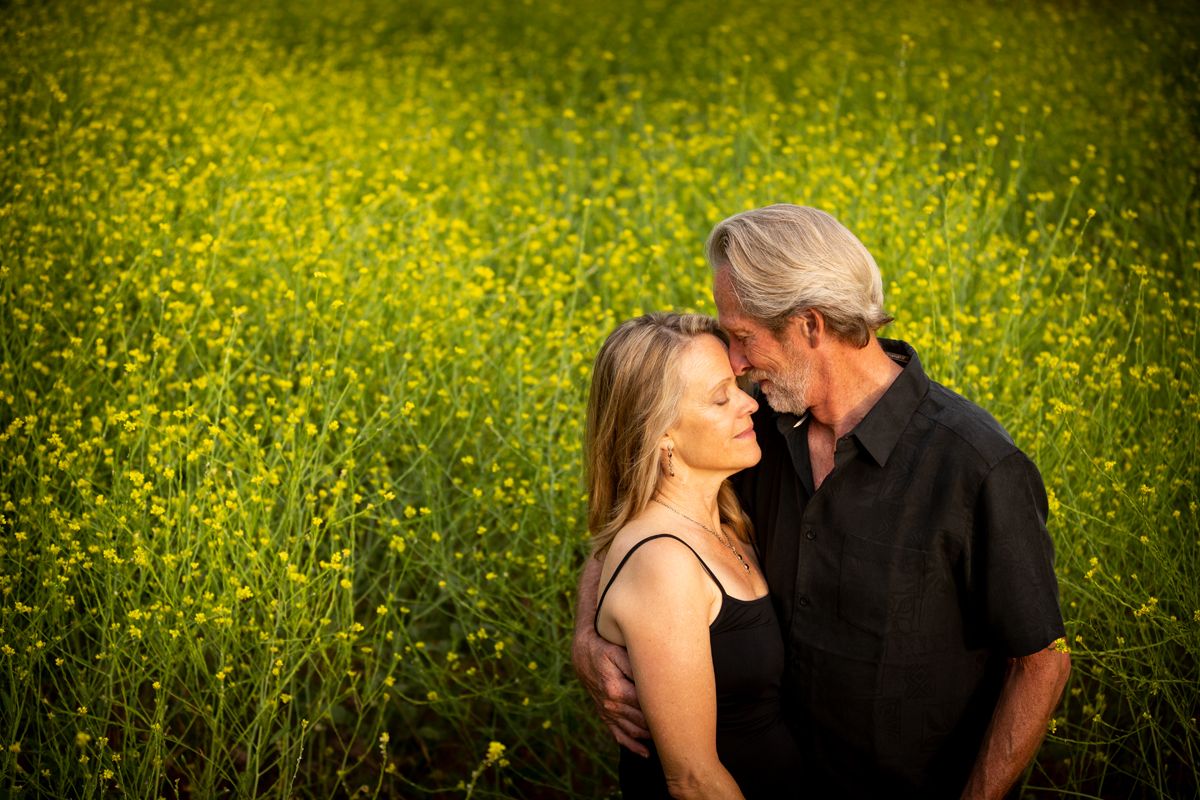 Couple sharing intimate moments in blooming yellow wildflower field during golden hour.