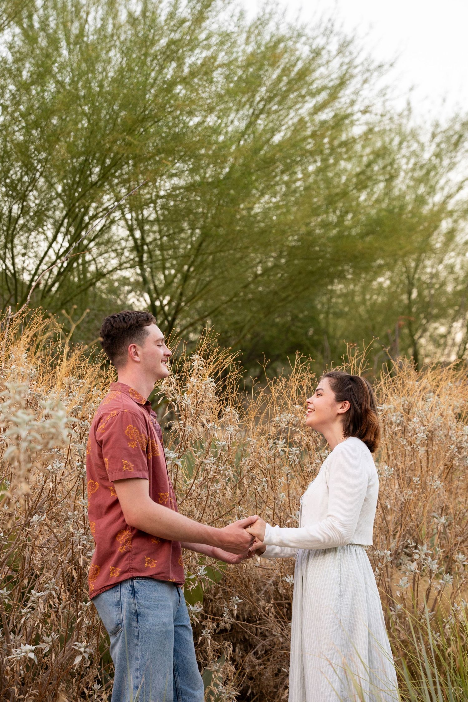 Two people share a candid moment while standing together in a field of tall, golden grass at sunset.