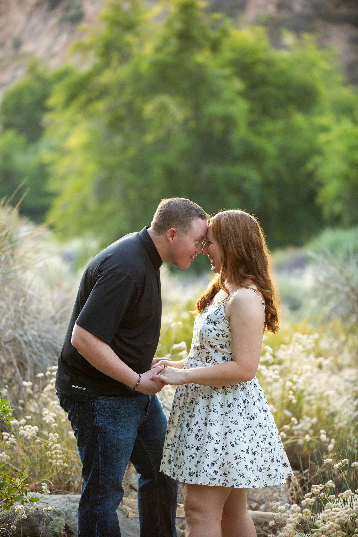A couple sharing an intimate kiss in a grassy field with summer wildflowers at sunset.