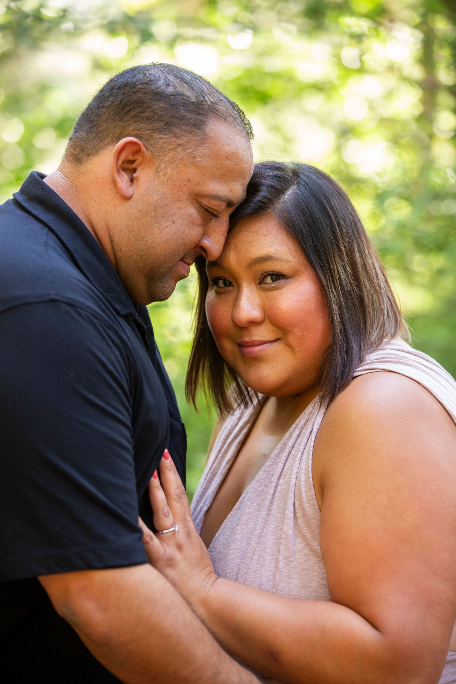 Loving couple shares an intimate outdoor moment in natural lighting with greenery in the background.
