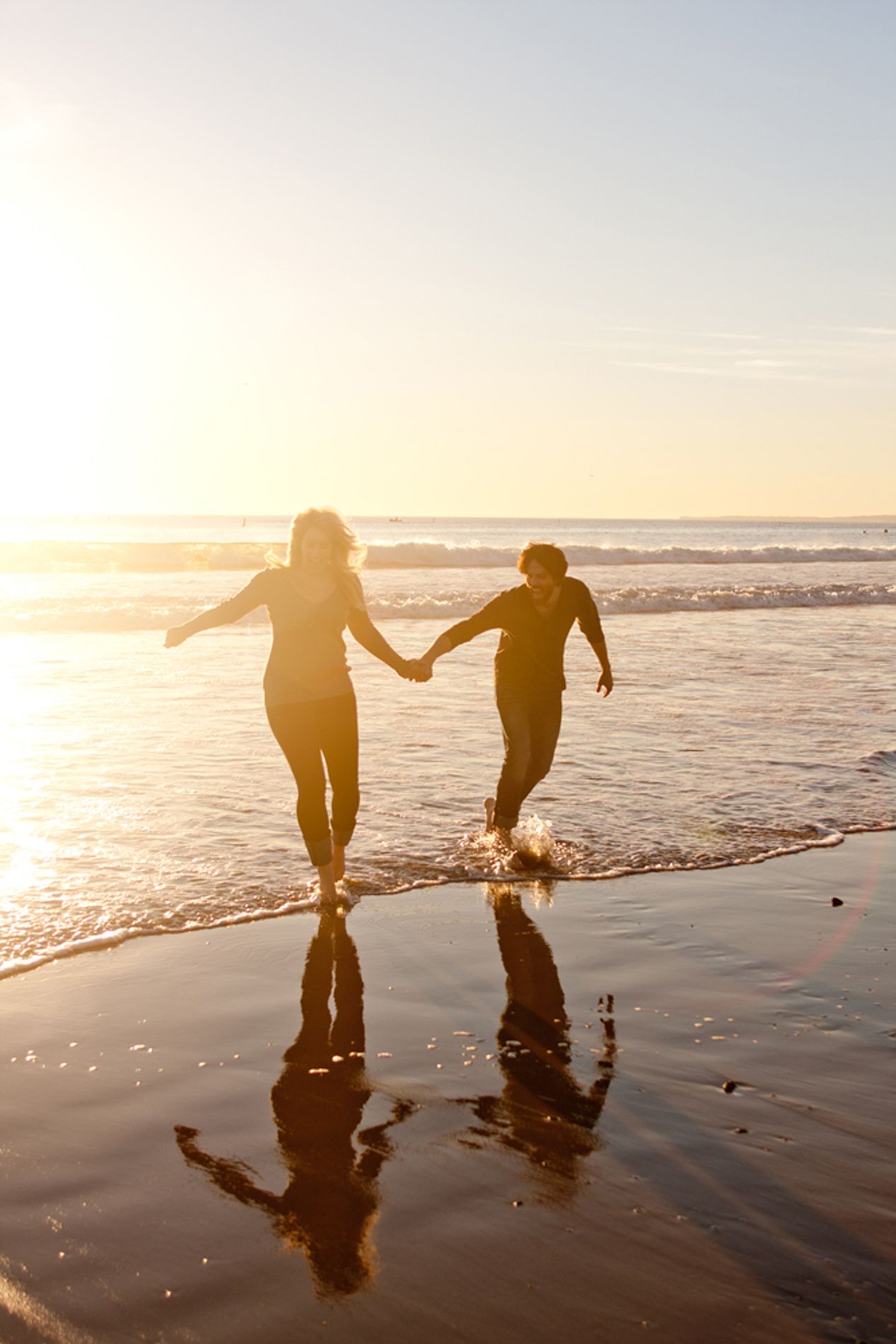 Silhouetted figures holding hands while running along beach shore at golden sunset.