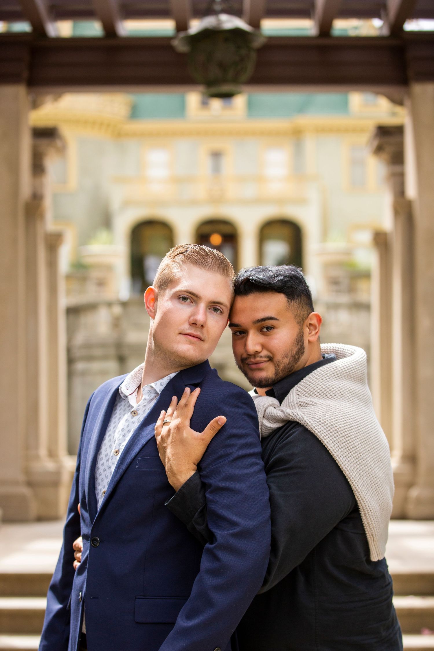 A couple in formal attire embraces under an ornate archway of a historic building.
