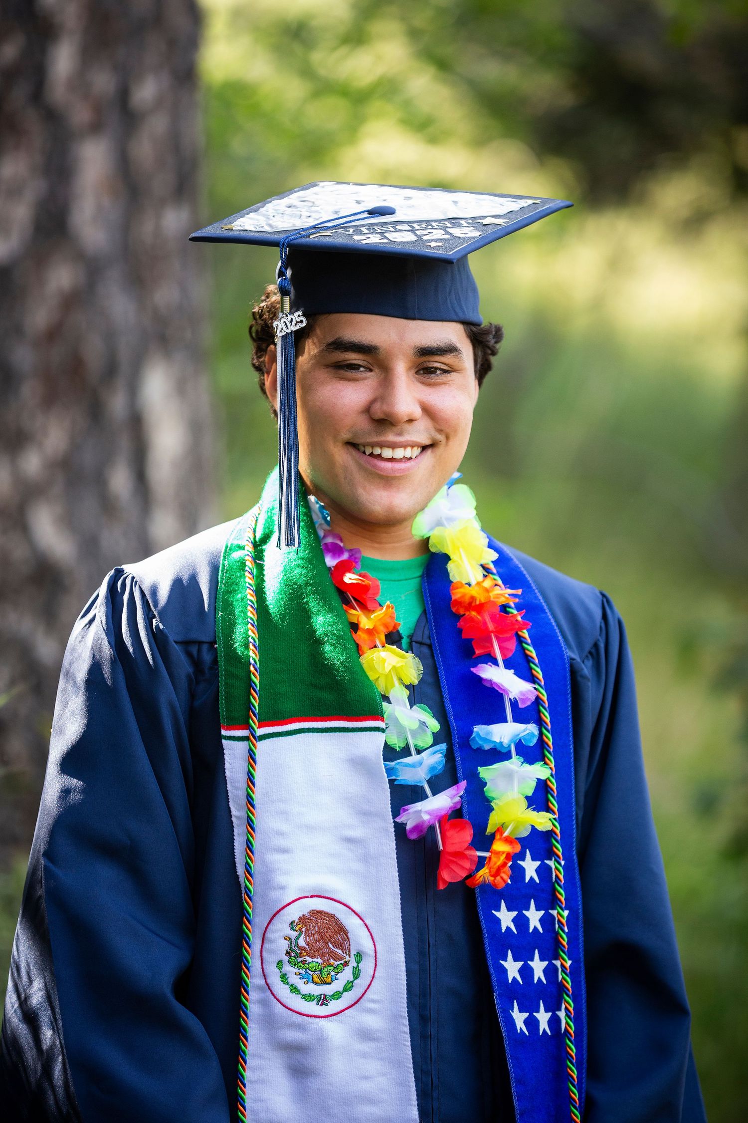 Graduate wearing colorful lei and Mexican flag graduation stole poses during outdoor graduation photo session.