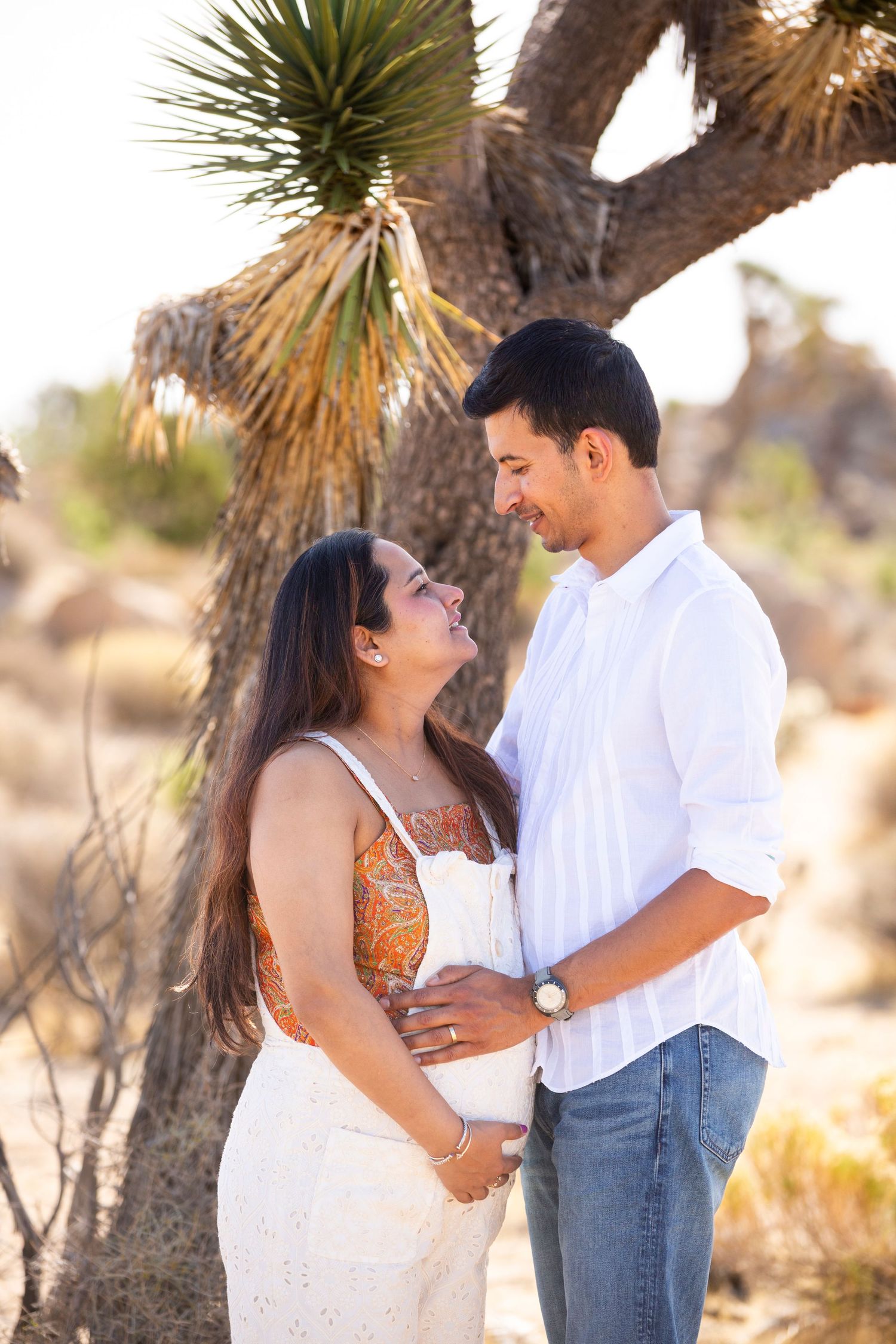 A couple shares an intimate moment together in a desert landscape with a Joshua tree in the background.