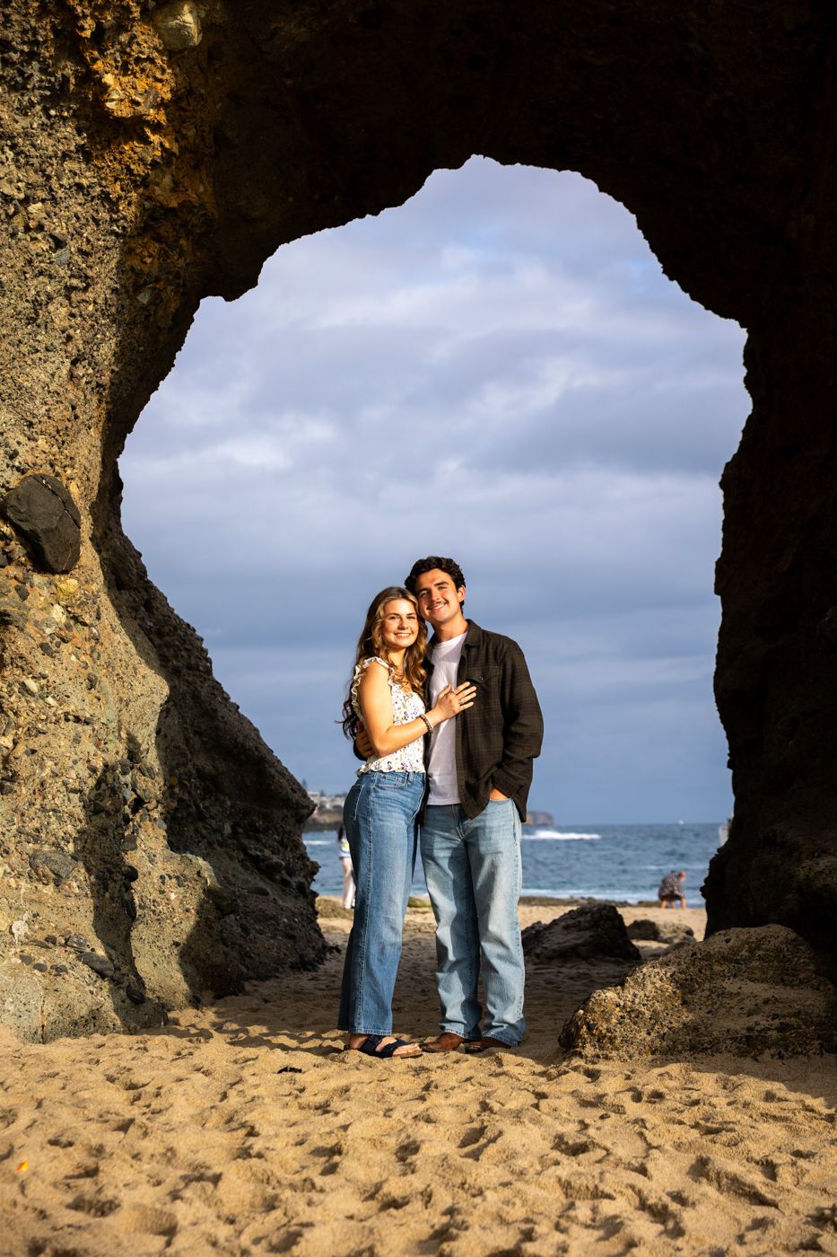 Natural rock arch frames graduates posing on sandy beach with ocean view. Beach photography, Huntington Beach, Laguna Beach, Redlands photo
