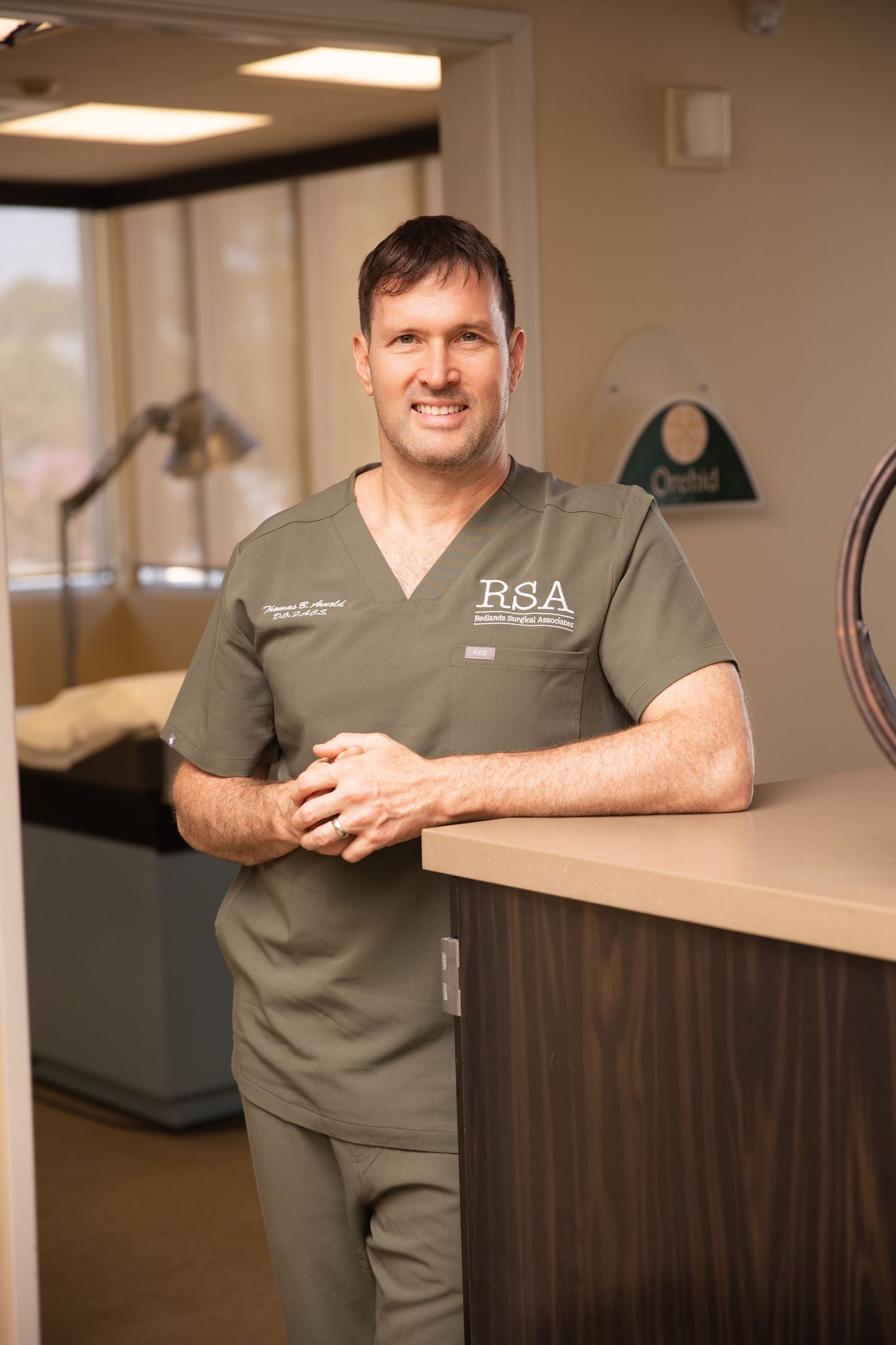 Medical professional in gray scrubs stands at counter in modern healthcare facility.