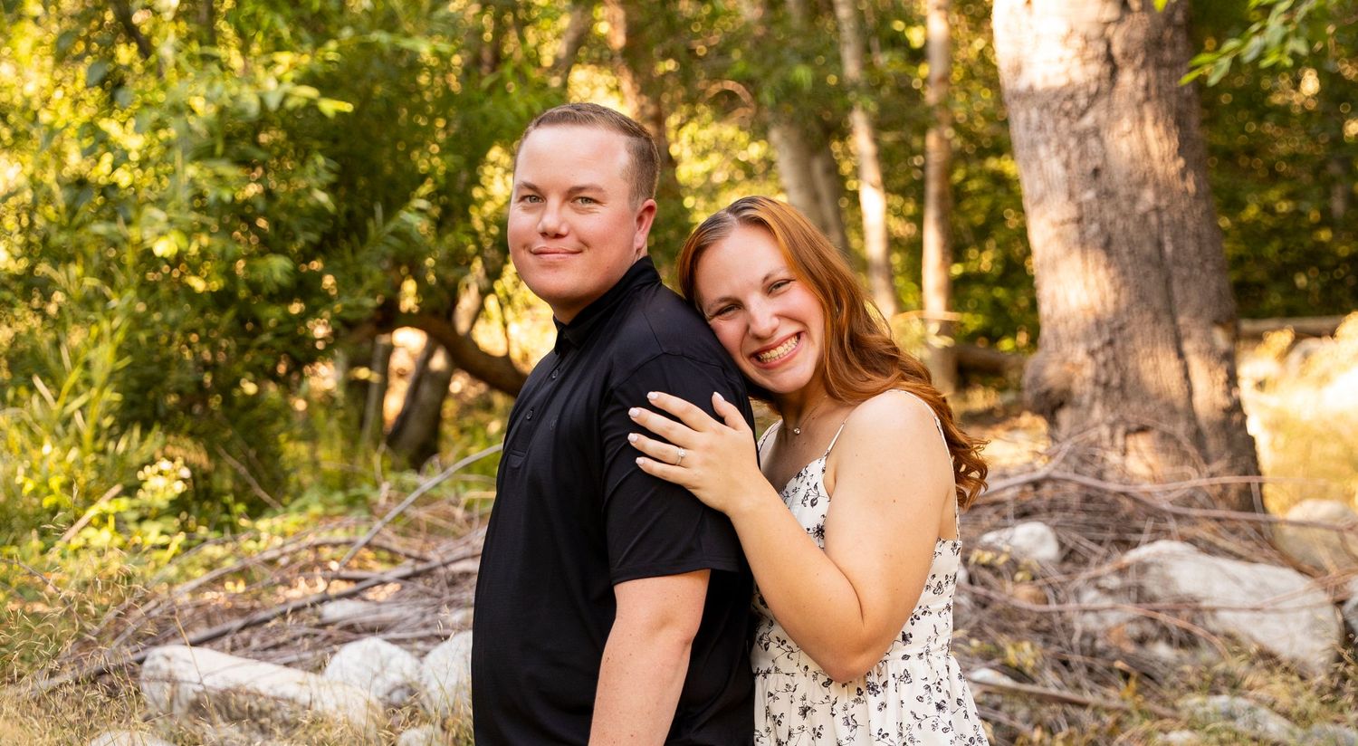 A romantic couple poses in an outdoor wooded setting during golden hour with beautiful natural lighting and foliage.