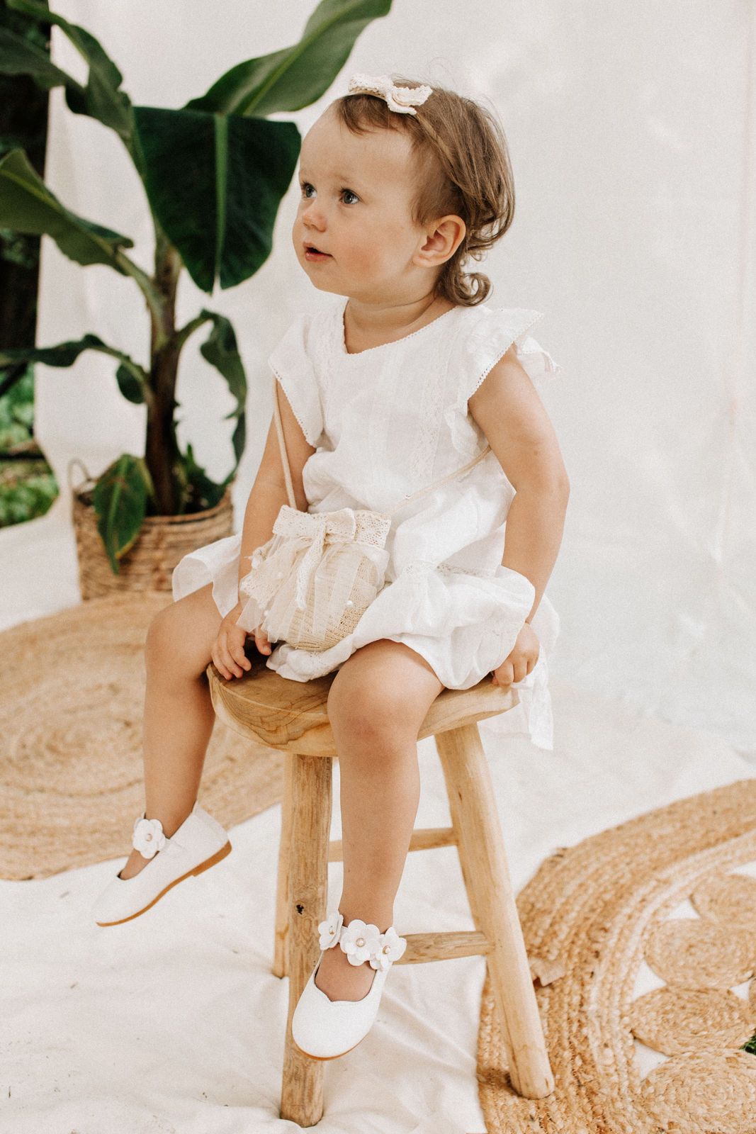 Kleines Mädchen in weißem Kleid sitzt auf einem Hocker