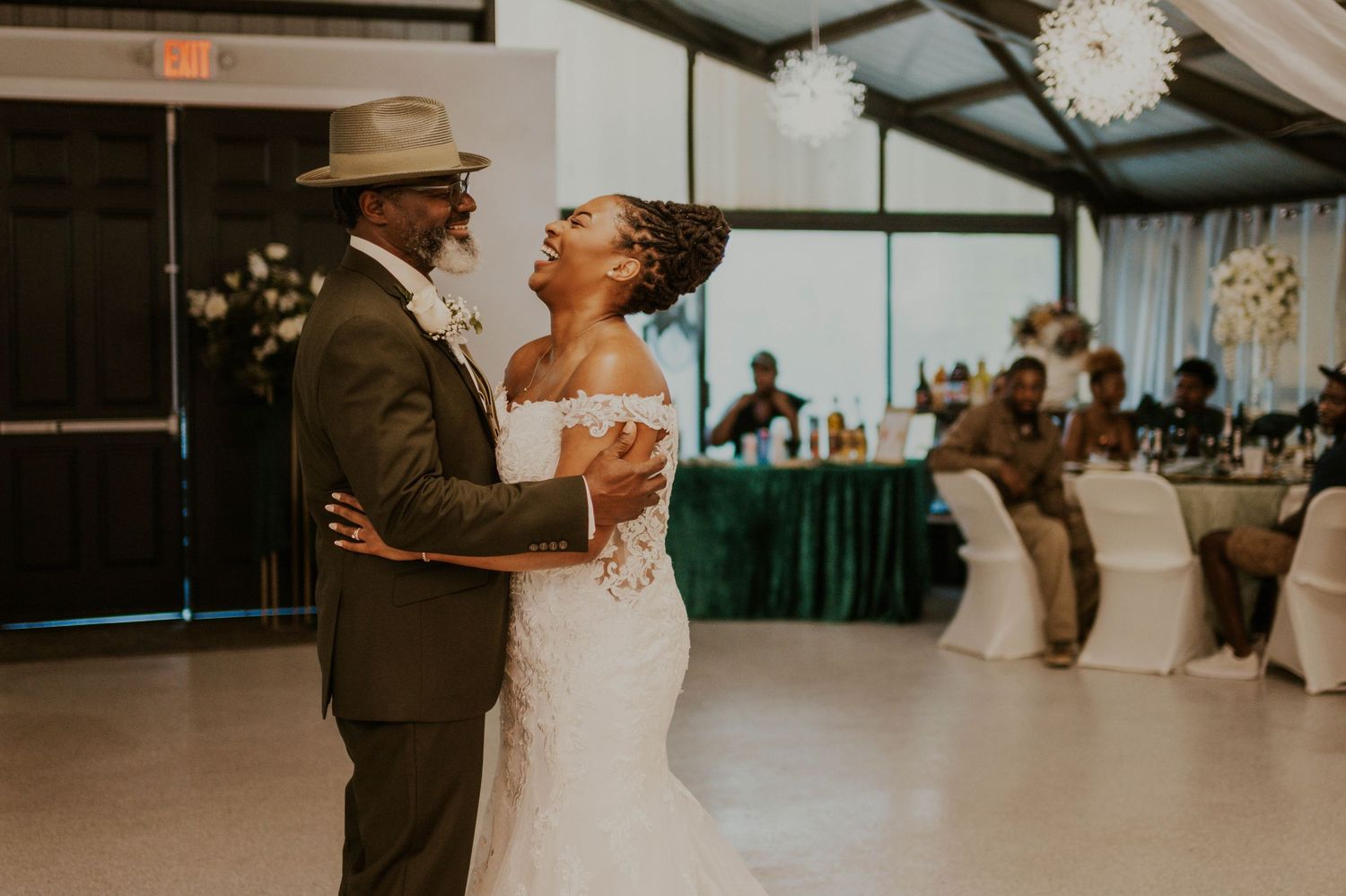 A bride and groom share their first dance at a wedding reception in an elegant venue with floral decorations.