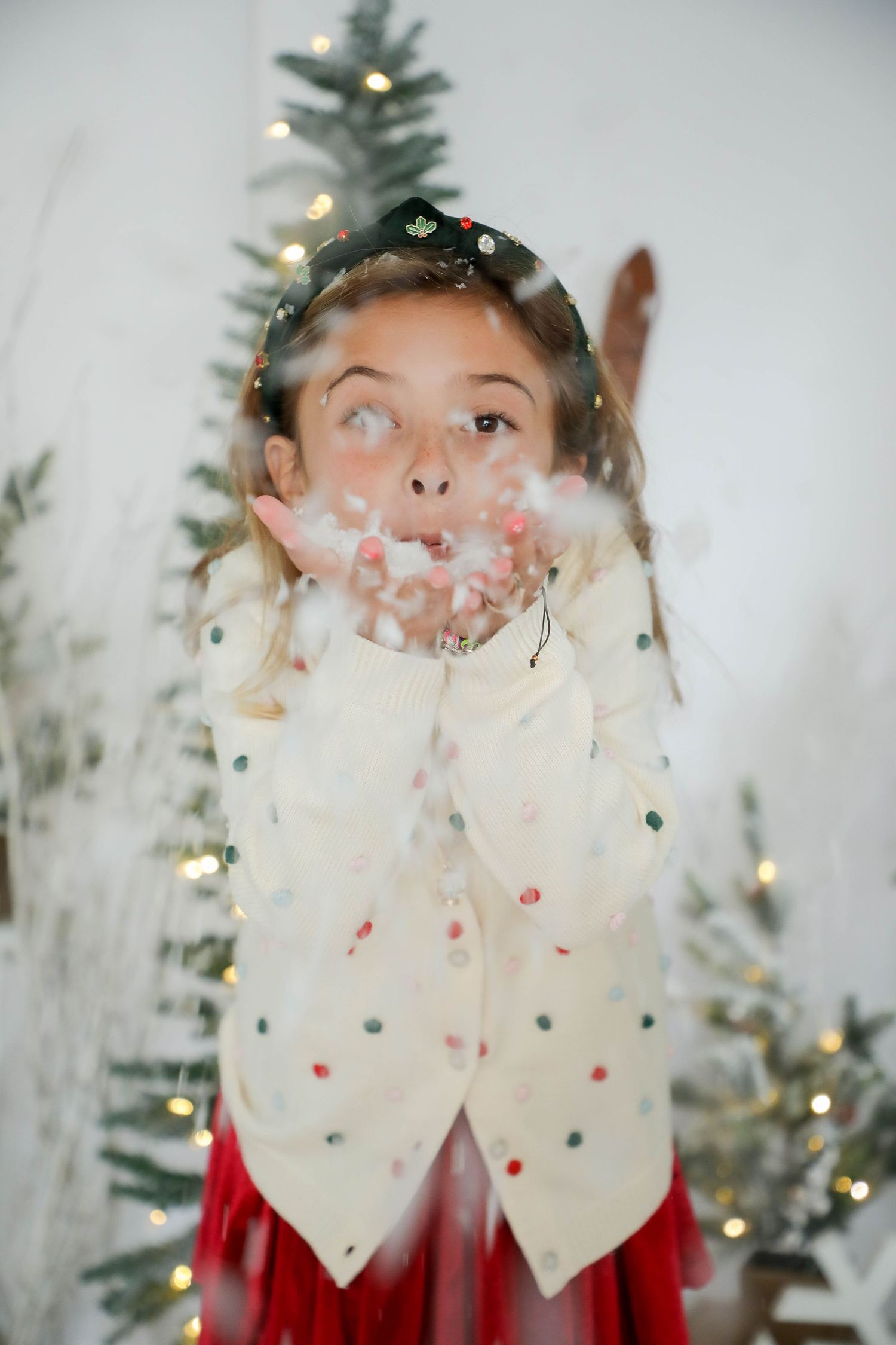 Winter portrait with white confetti and twinkling holiday lights against a Christmas tree backdrop.