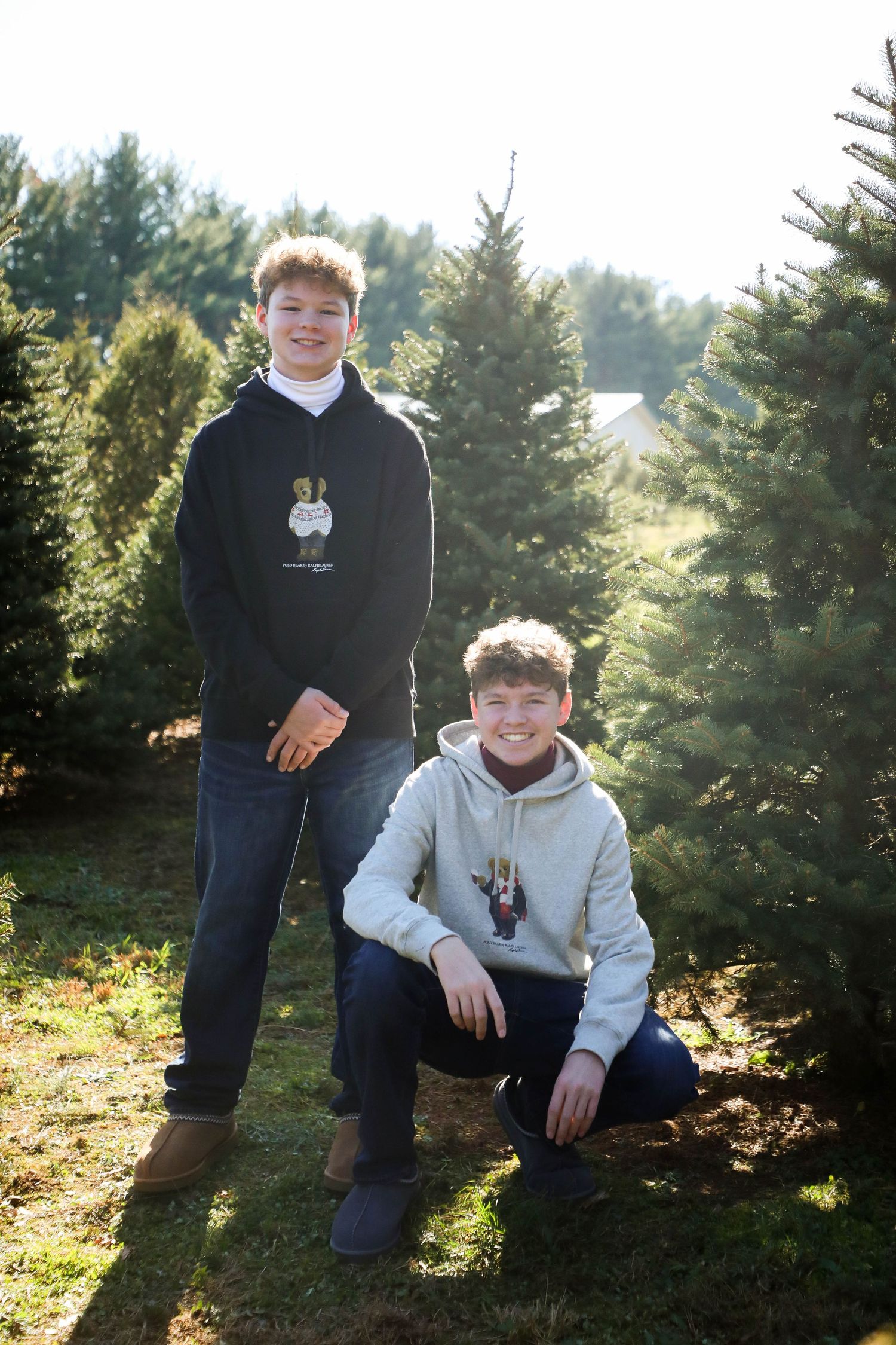 Two youths posing together among evergreen trees on a sunny day.