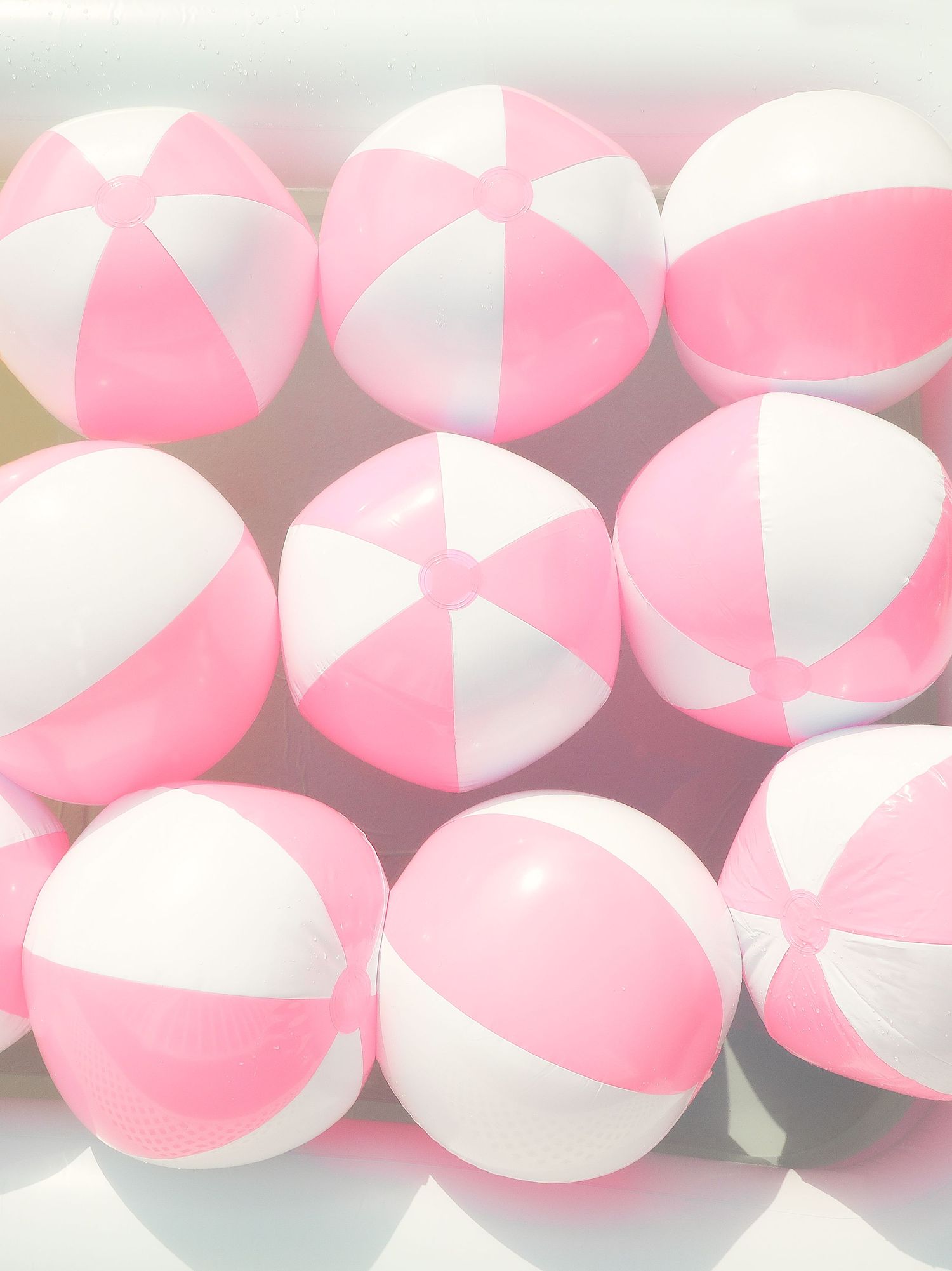 Pink and white striped beach balls lined up in rows create a repeating pattern on a gray surface.