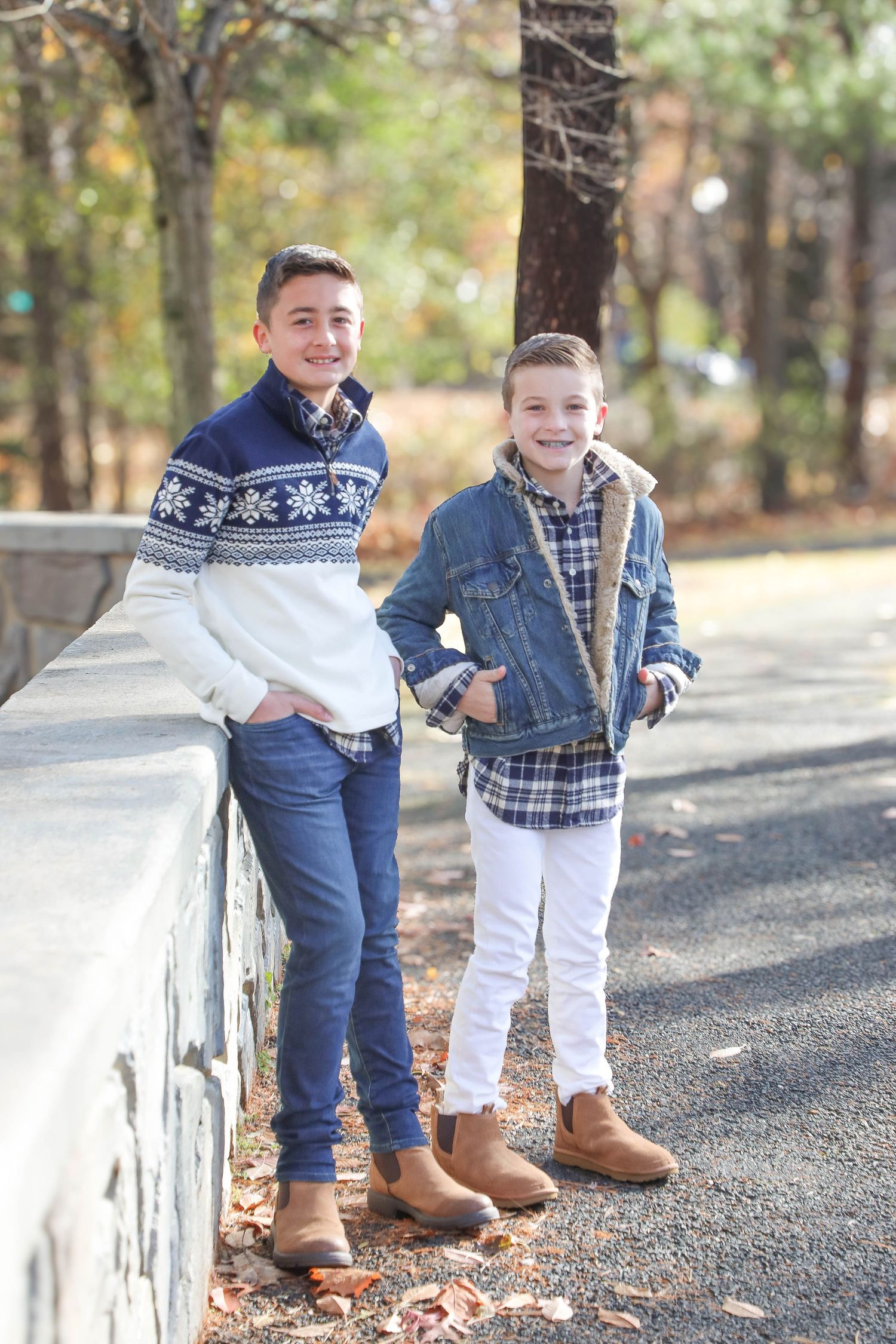 Two young people in casual fall attire leaning against a stone wall outdoors.