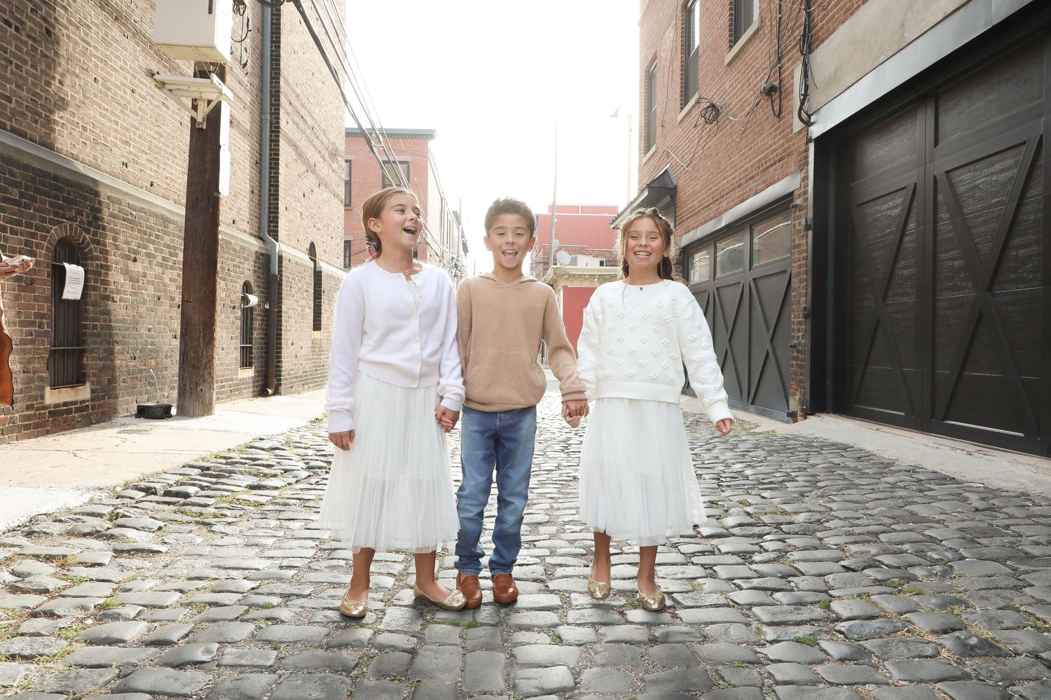 Three people walking together on a cobblestone street between brick buildings.