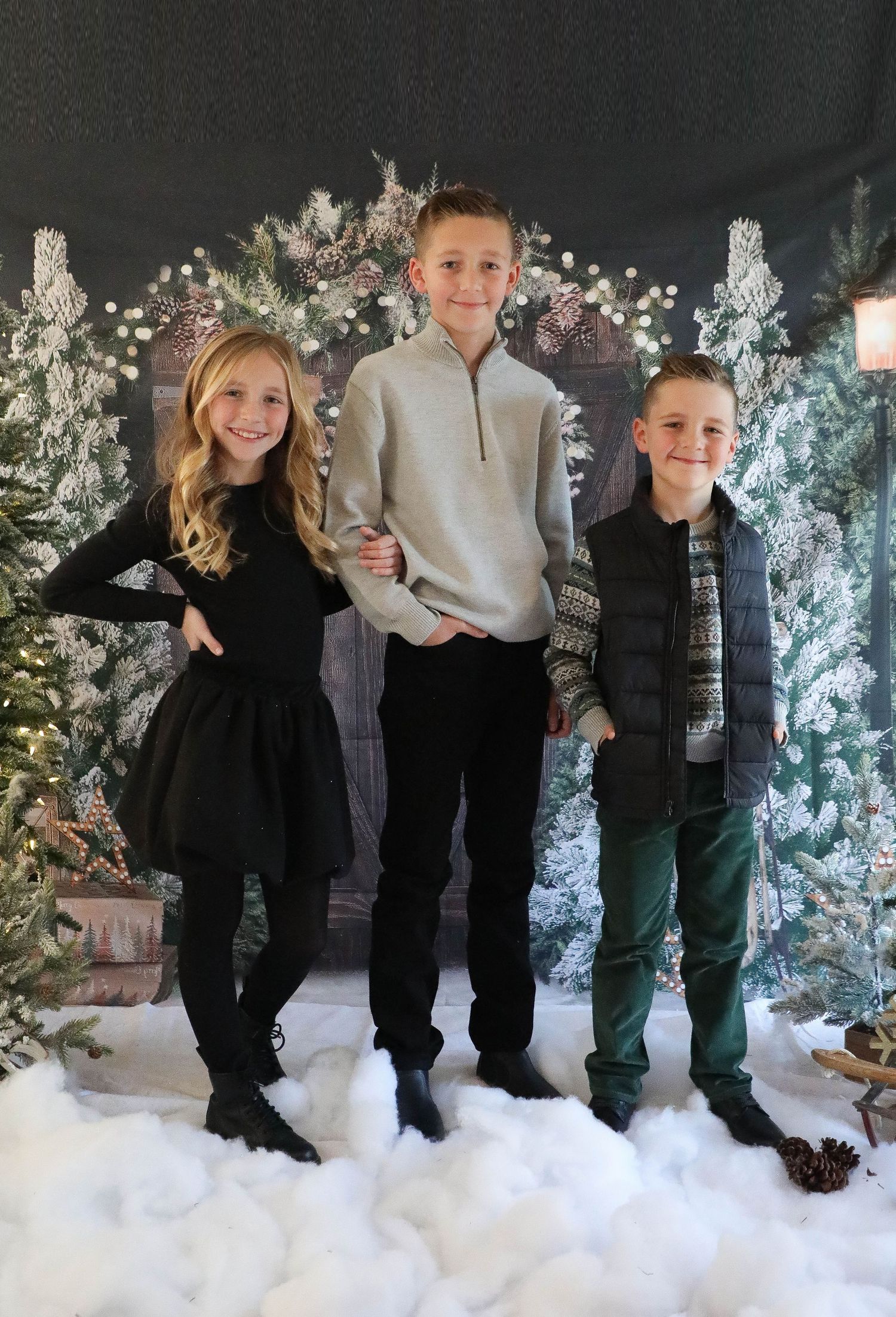 Holiday portrait with three siblings against snowy winter scene with sparkling lights.
