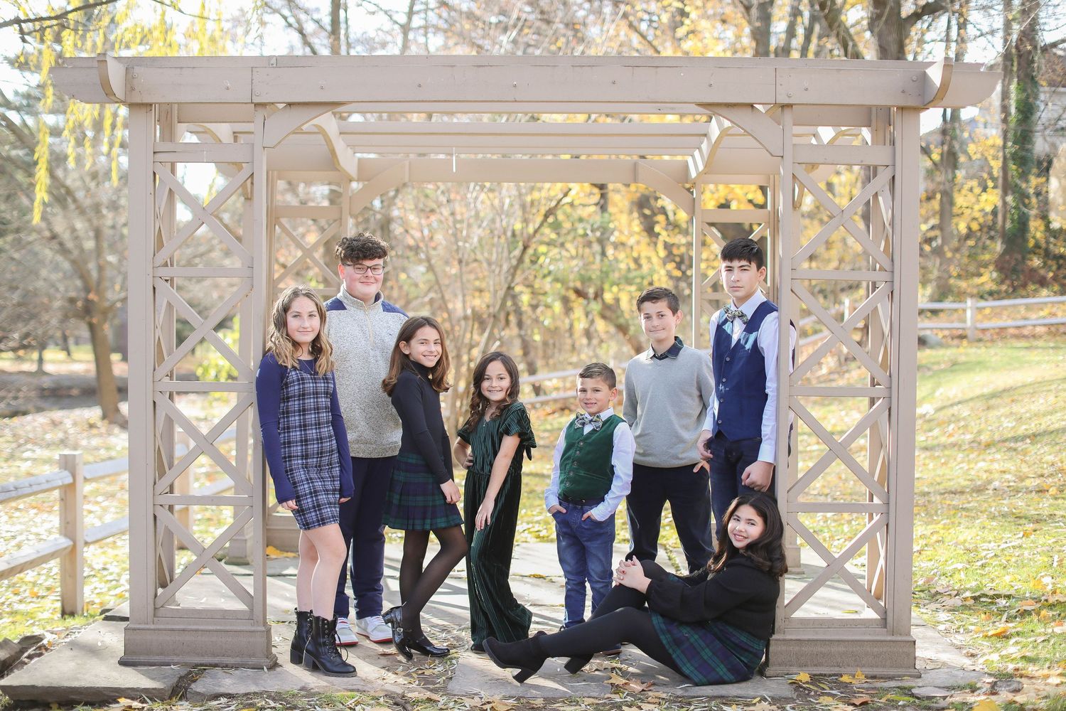 Group of students pose together under wooden pergola in fall outdoor setting.