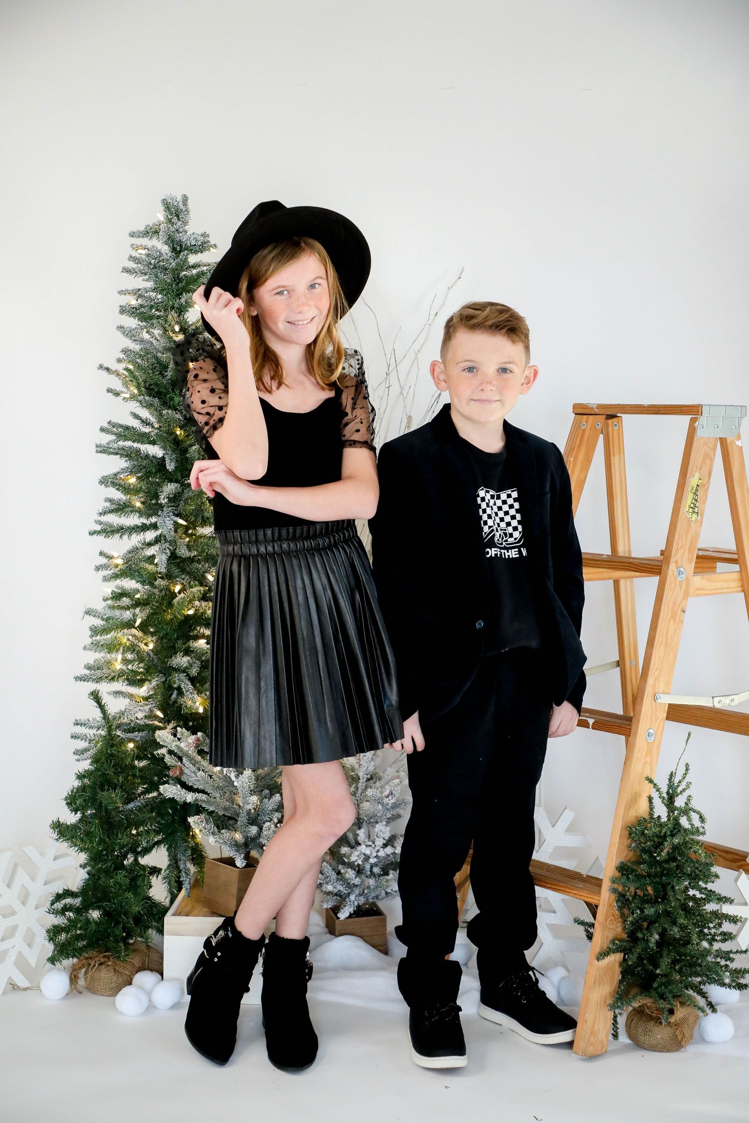 Festive holiday portrait with Christmas trees and wooden ladder in white studio setting.