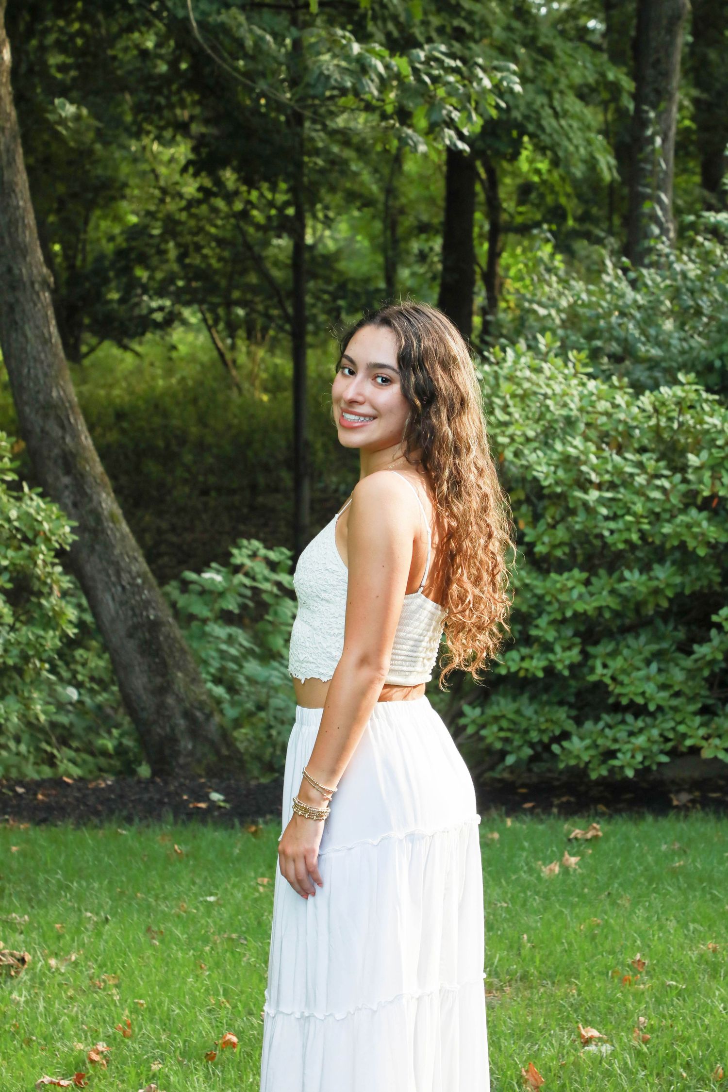 Woman in white two-piece dress poses gracefully in garden setting.