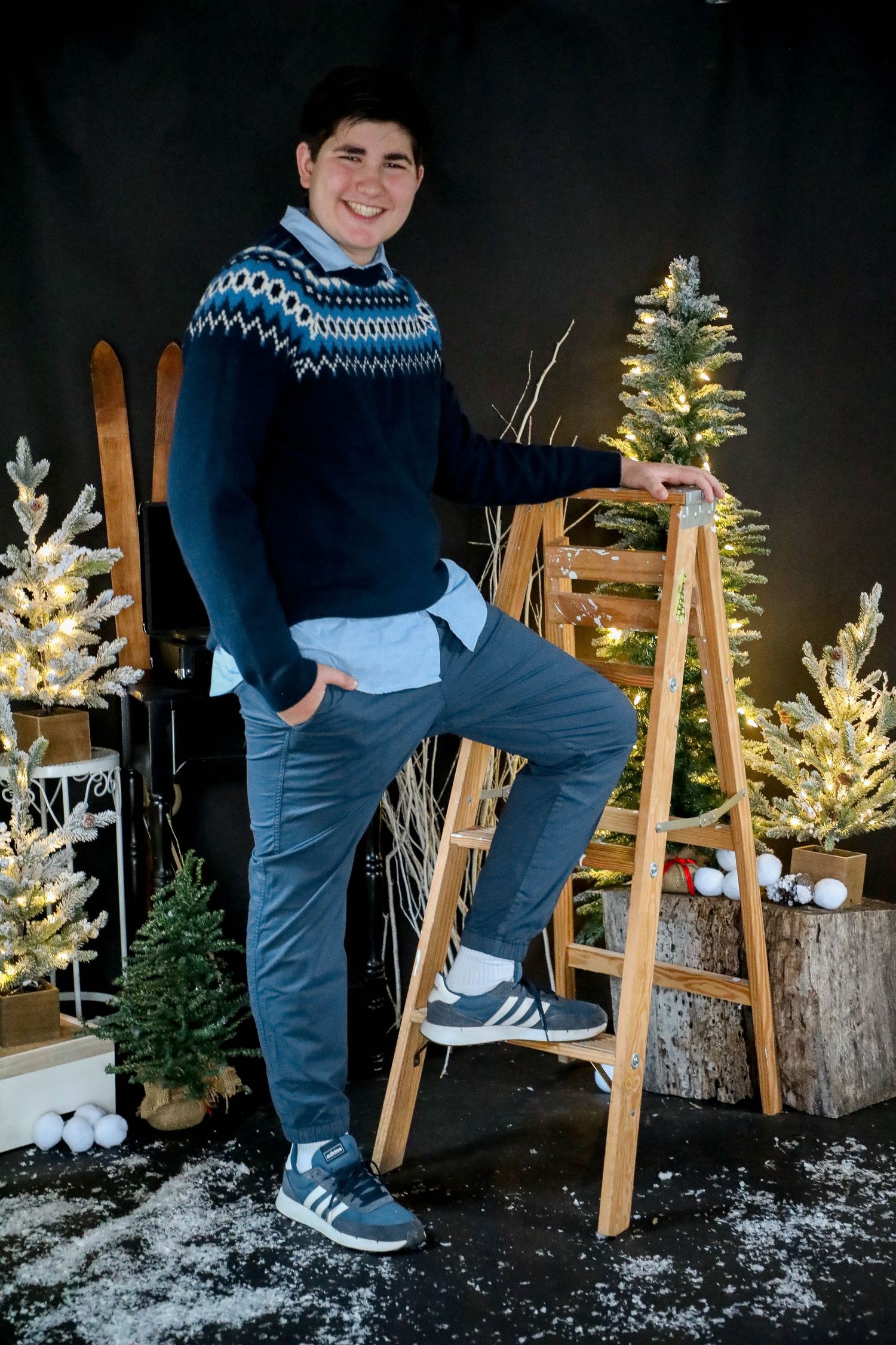 Person in blue Fair Isle sweater standing on wooden ladder against Christmas trees.