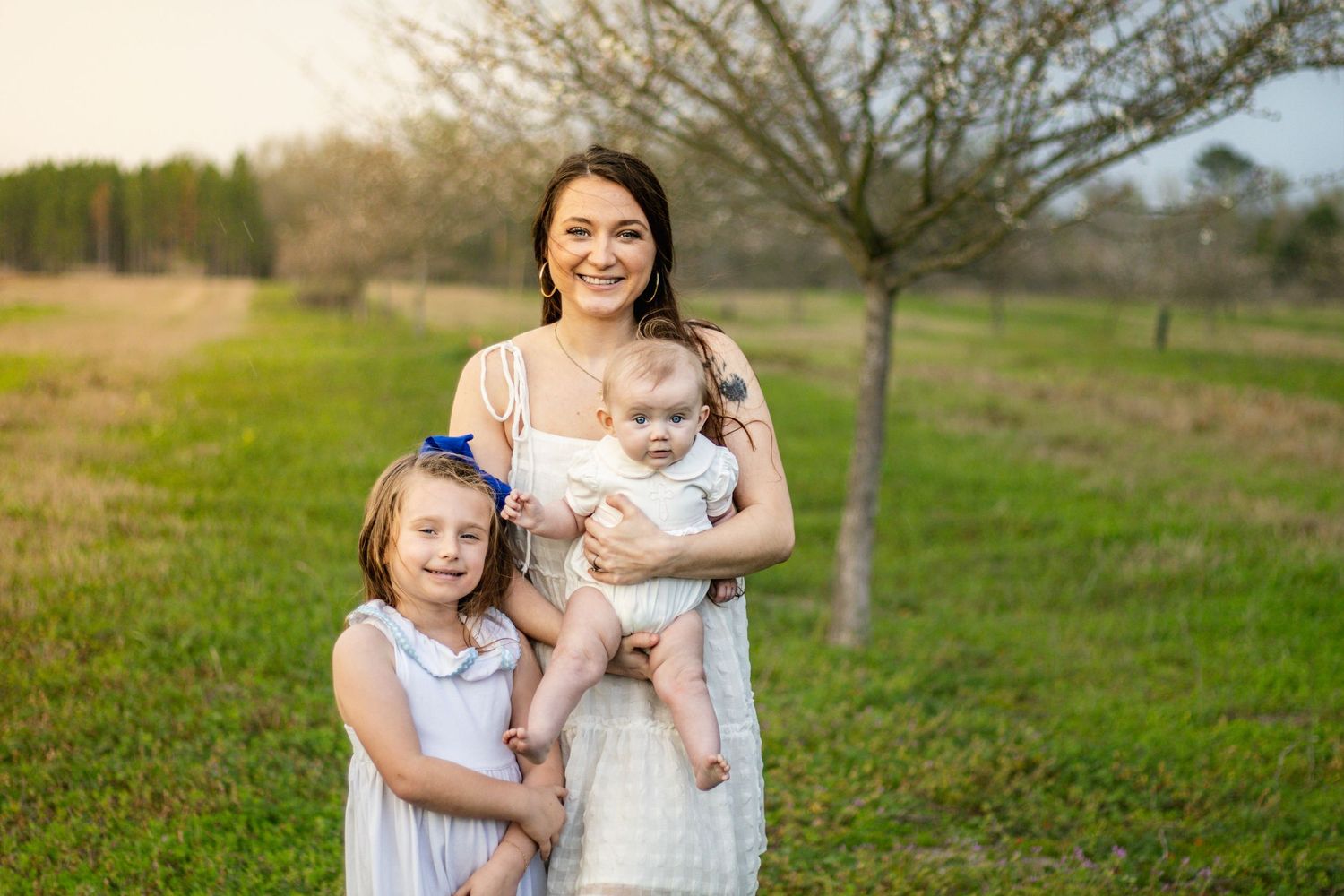 Smiling mother holding baby while standing with young daughter outdoors.