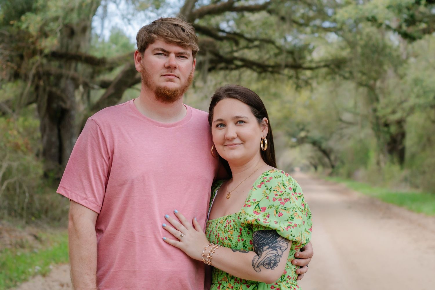 Close-up of a couple on a tree-lined dirt road, woman in green floral dress resting hand on mans chest.