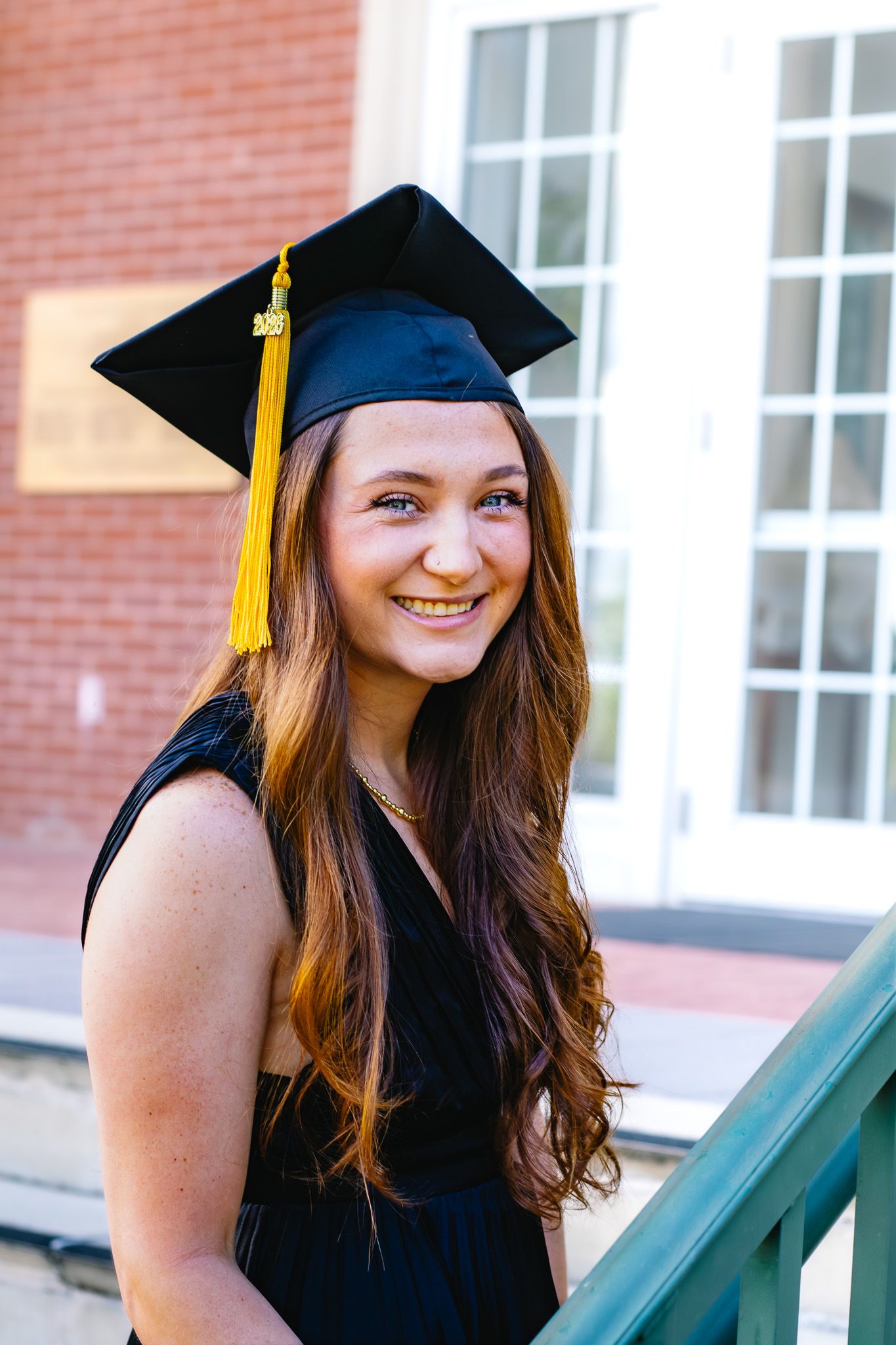 Smiling graduate in black cap with gold tassel and black dress.