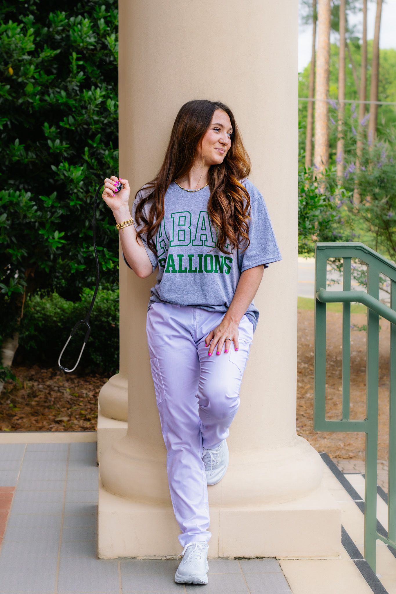 Woman in ABAC Stallions tee and lavender pants poses confidently against a white column outdoors.