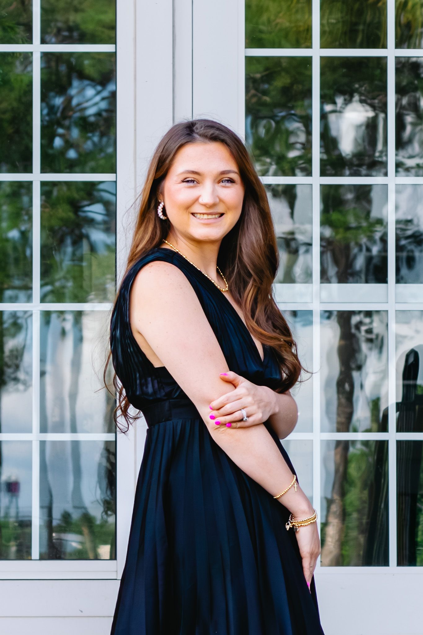 Young woman in black dress smiling outdoors near white window.