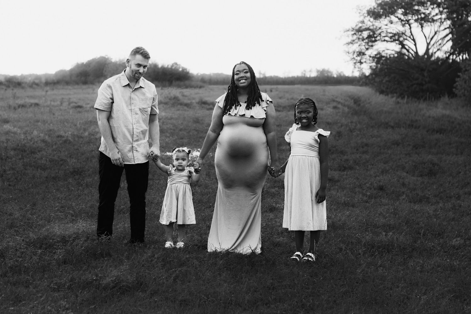 Black and white photo of interracial family holding hands together in an open grassy field.