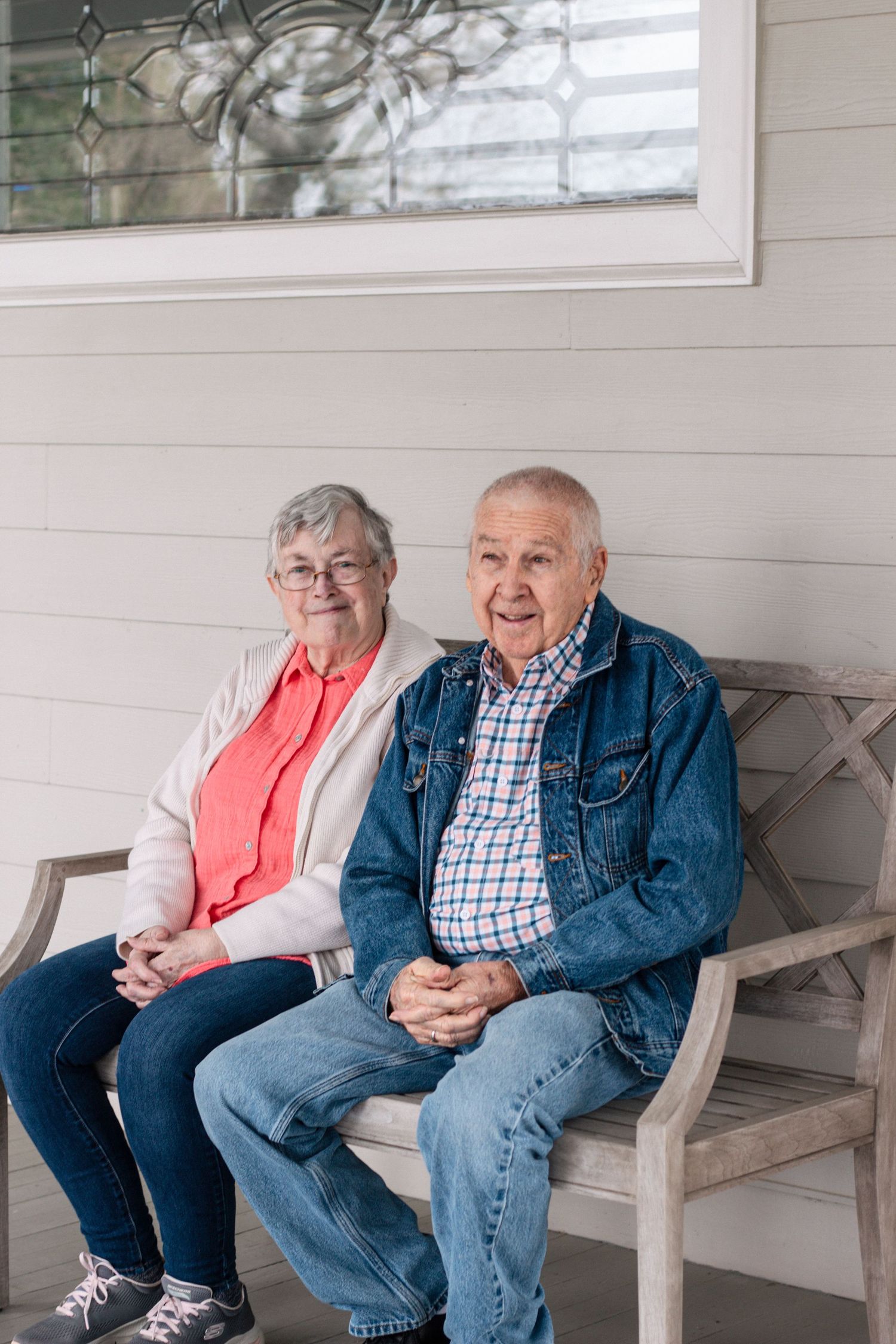 Senior couple sitting on a bench on a porch, smiling at the camera together.