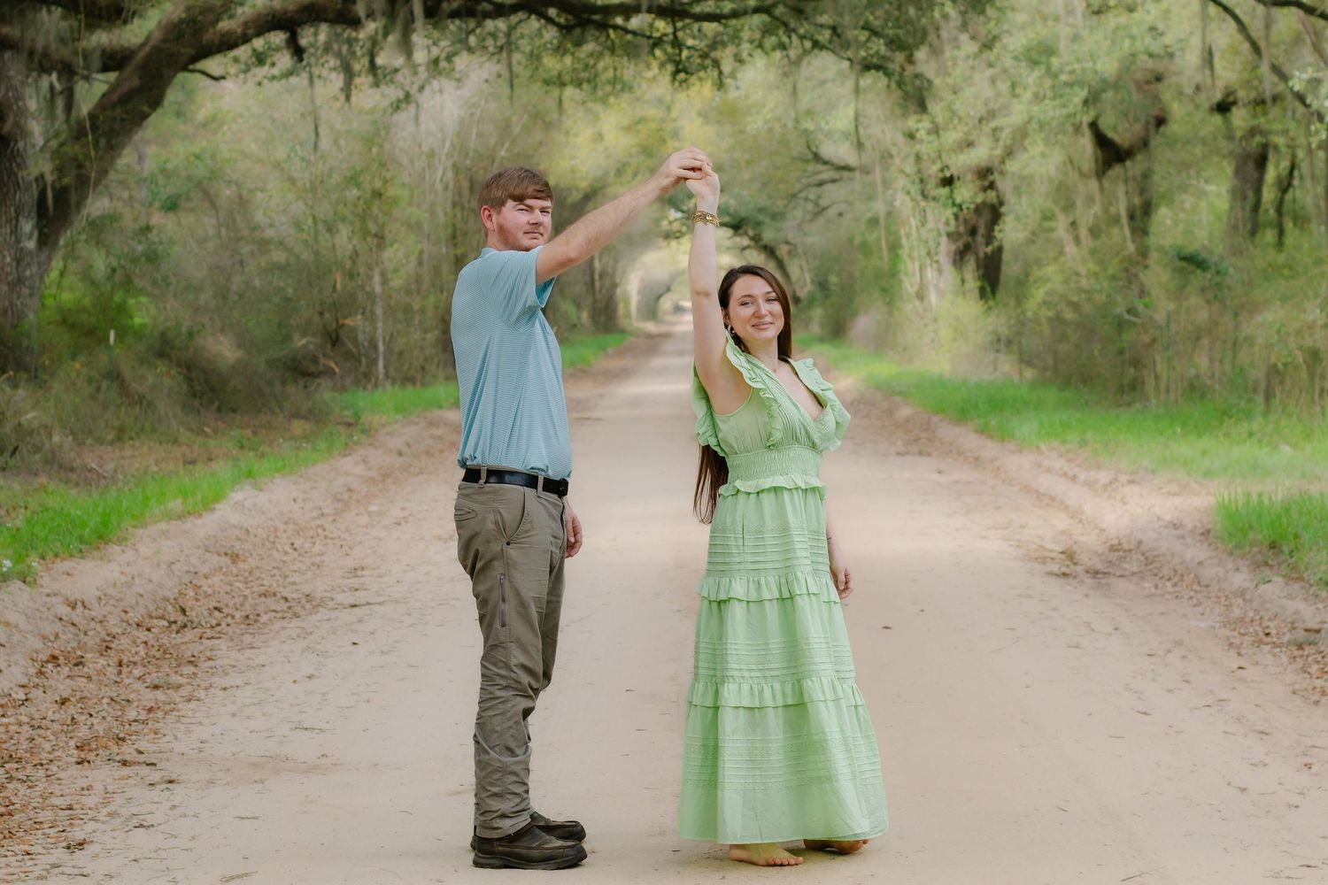 Couple dancing on a scenic tree-lined dirt road, man in blue polo spinning woman in green dress.