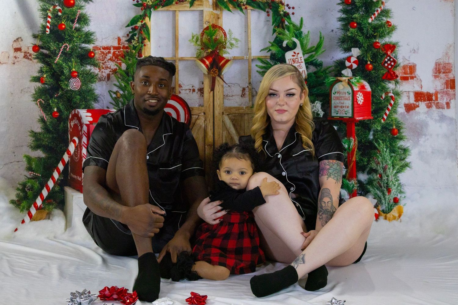 Family of three in holiday attire posing together in front of a decorated Christmas backdrop with festive ornaments.