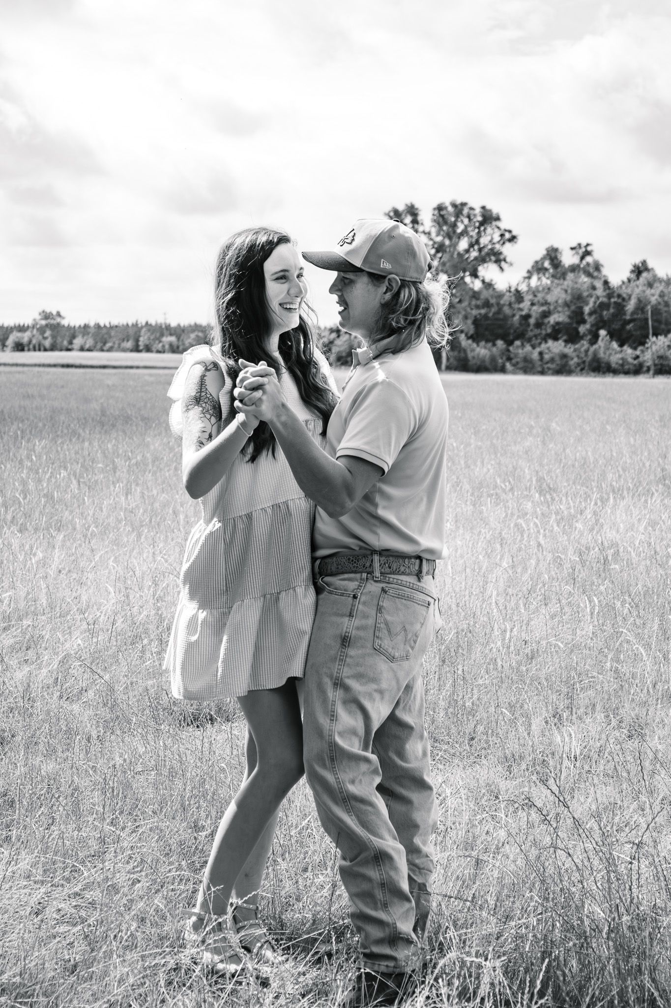 Black and white photo of a couple dancing together in an open grassy field under a cloudy sky.