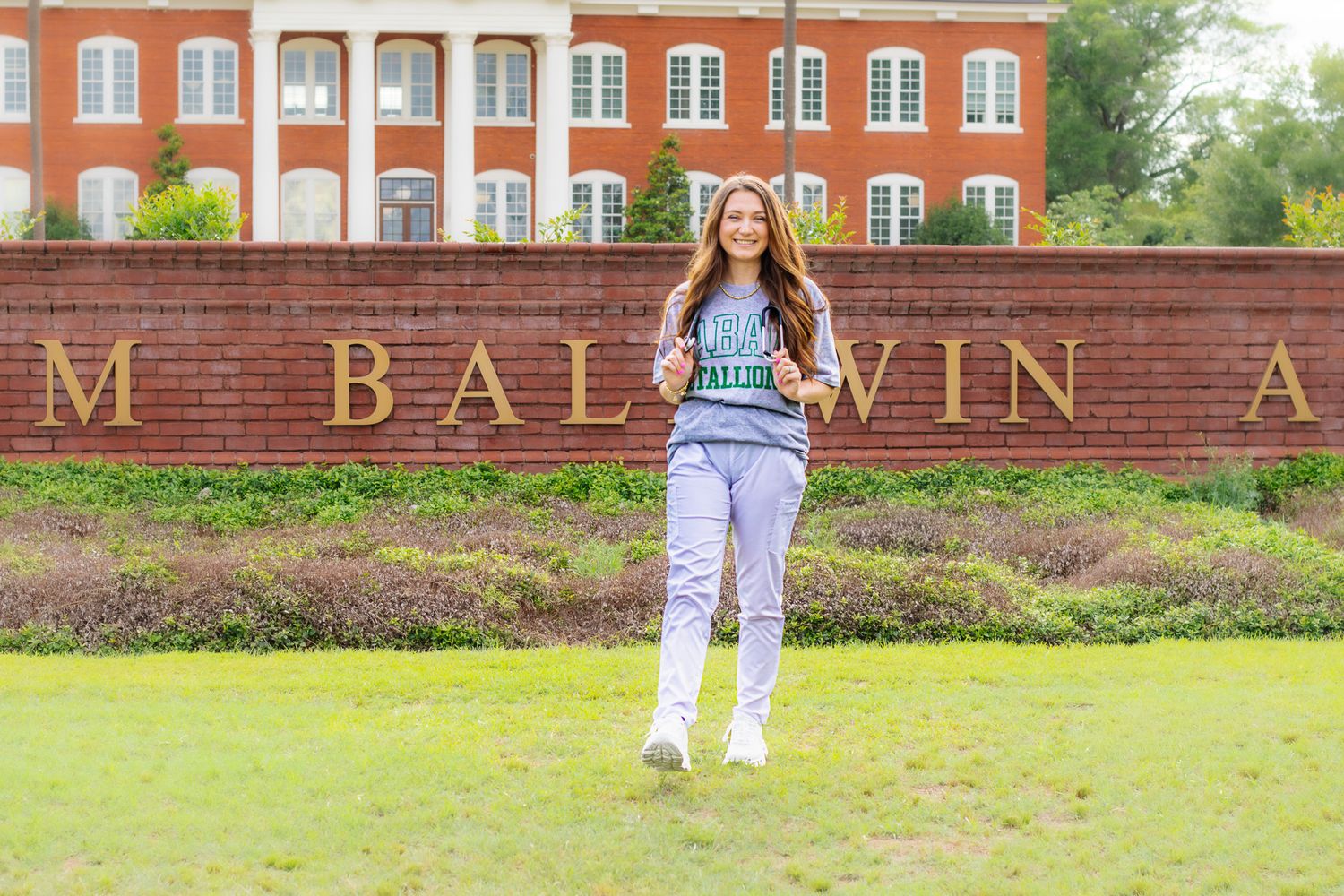 Young woman in college shirt walks in front of Baldwin Academy brick sign outdoors.