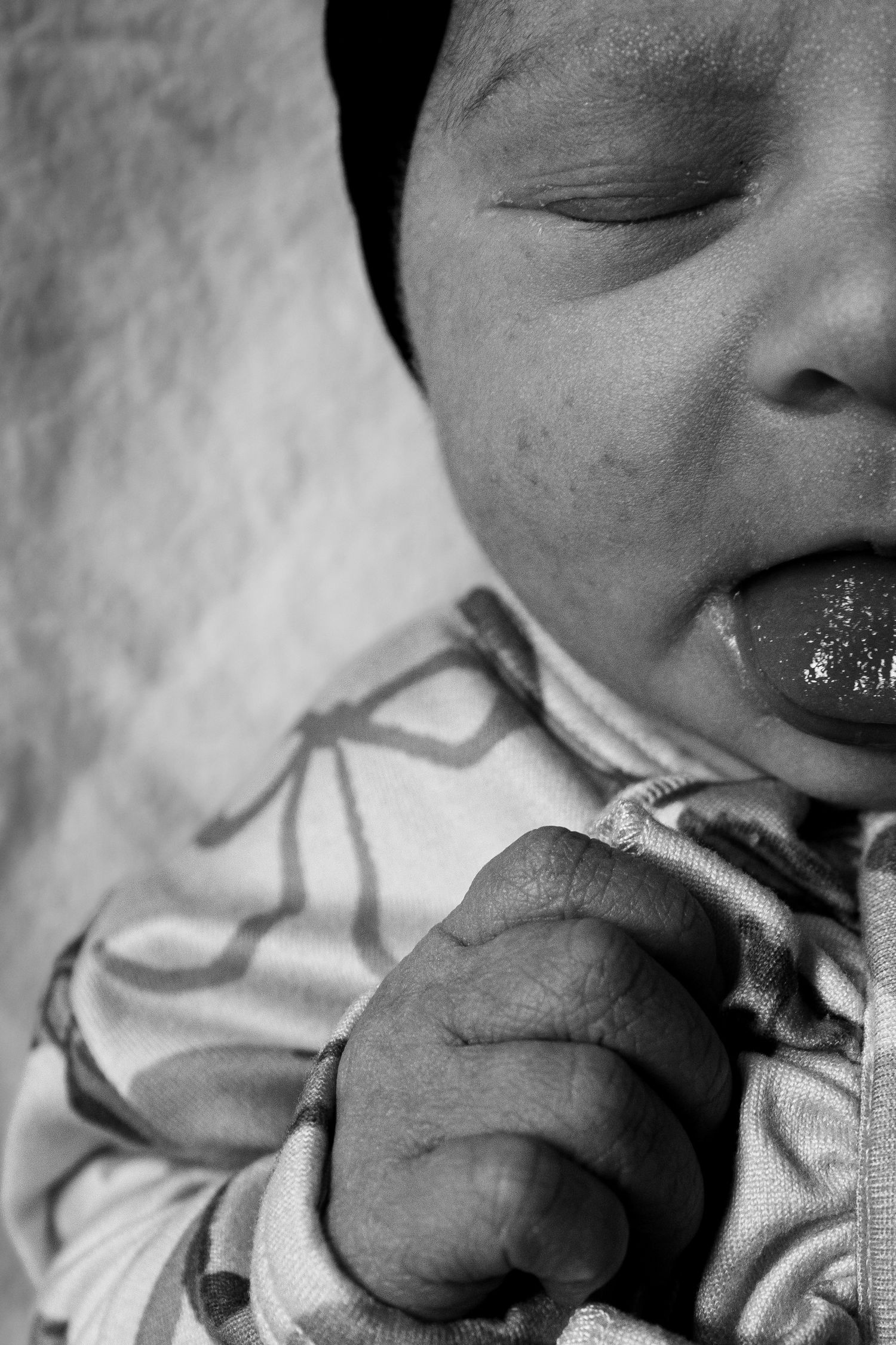 Black and white close-up of sleeping newborn baby with mouth slightly open.