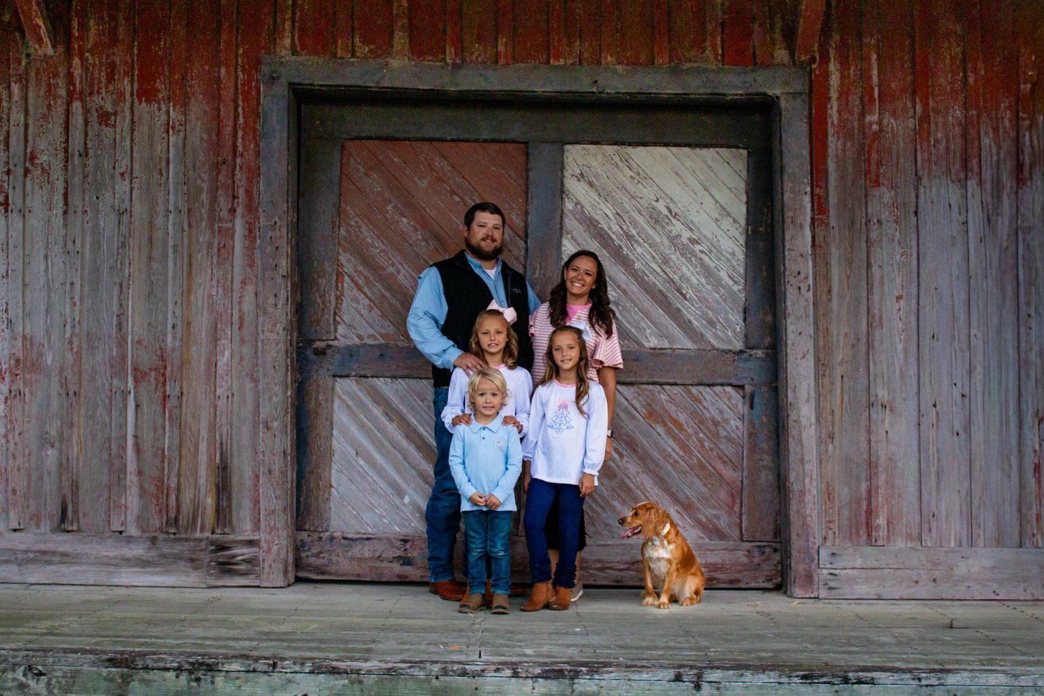 Family of five with a dog posing in front of a rustic barn door.