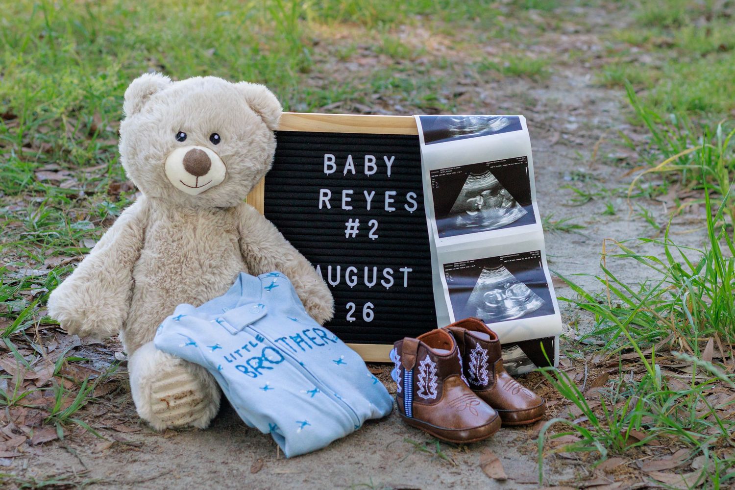 Baby Reyes number 2 gender reveal flat lay with teddy bear, blue onesie, boots, and ultrasound photos.