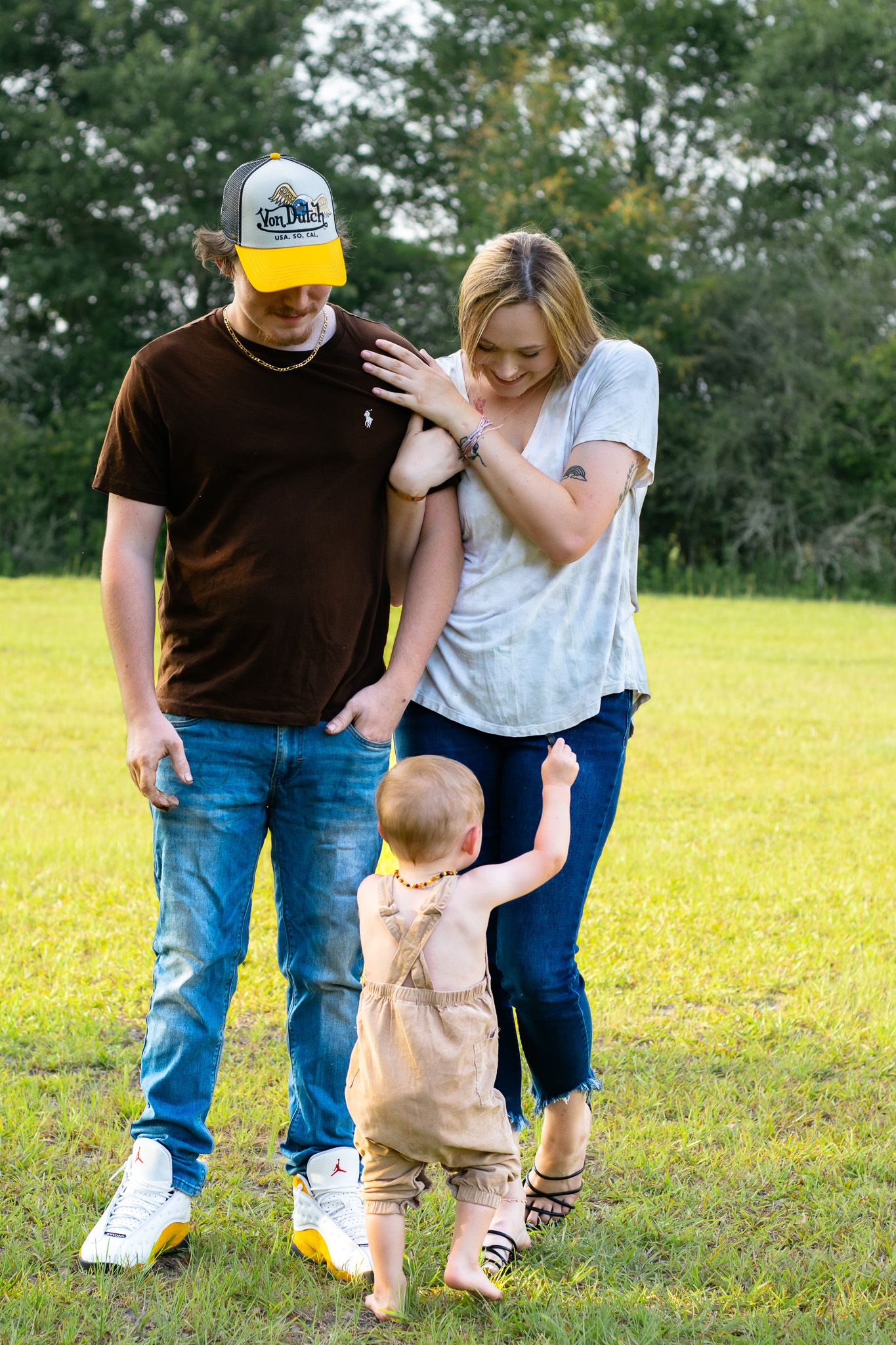 Young family with toddler playing outdoors on green grass field on a sunny day.