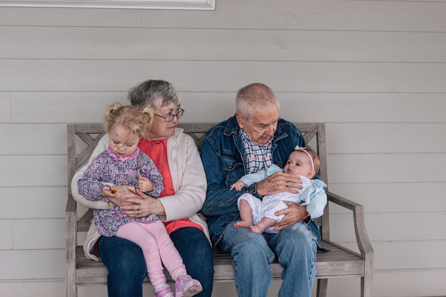 Grandparents sitting on a bench, each lovingly holding a young grandchild, sharing a tender moment.