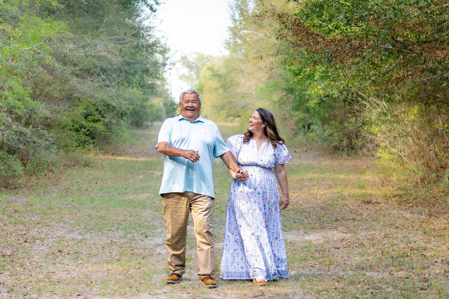 Happy older couple walking hand in hand along a scenic wooded trail on a sunny day.