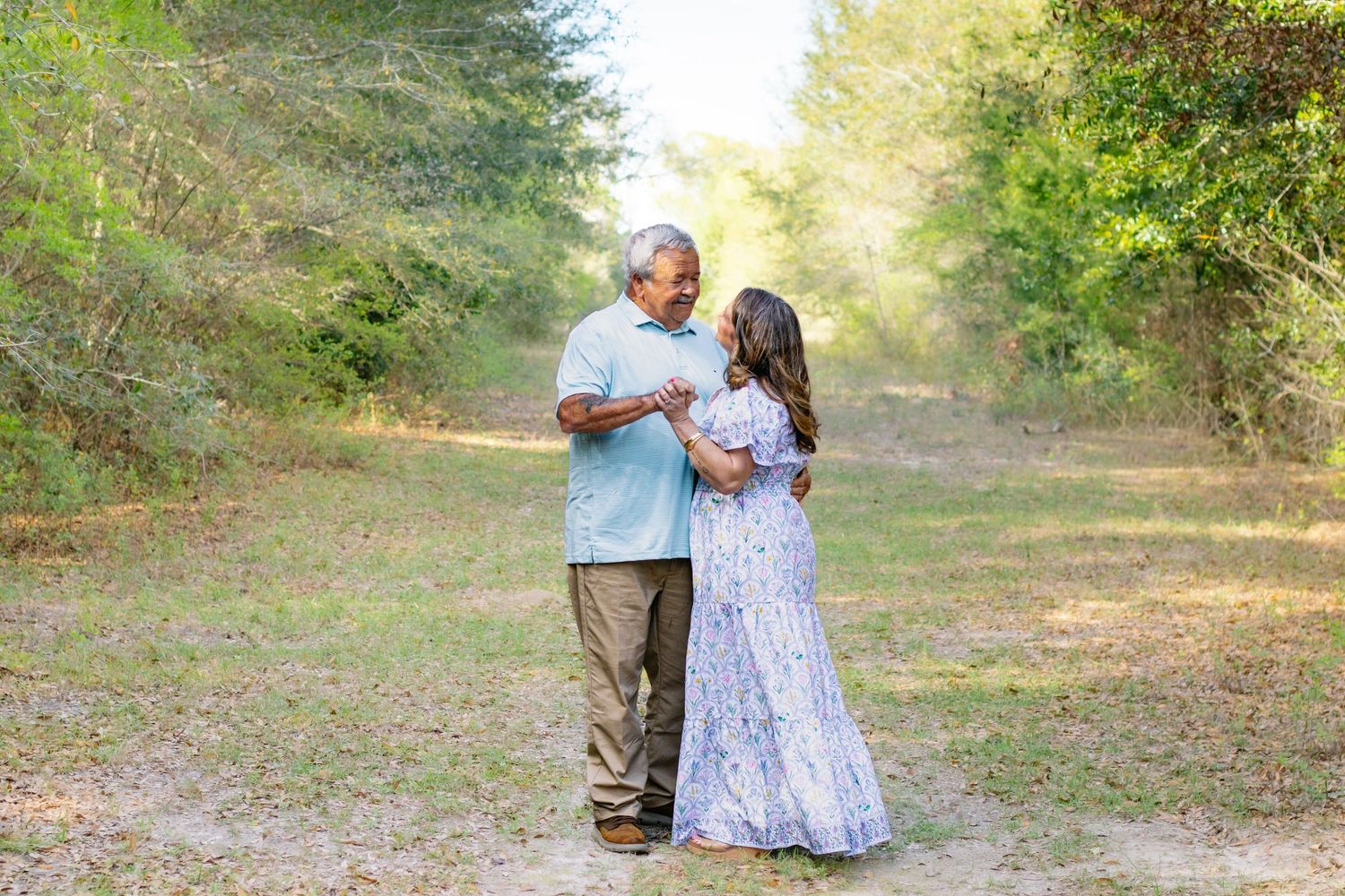 Older couple sharing a sweet moment together on a grassy path surrounded by lush green trees.