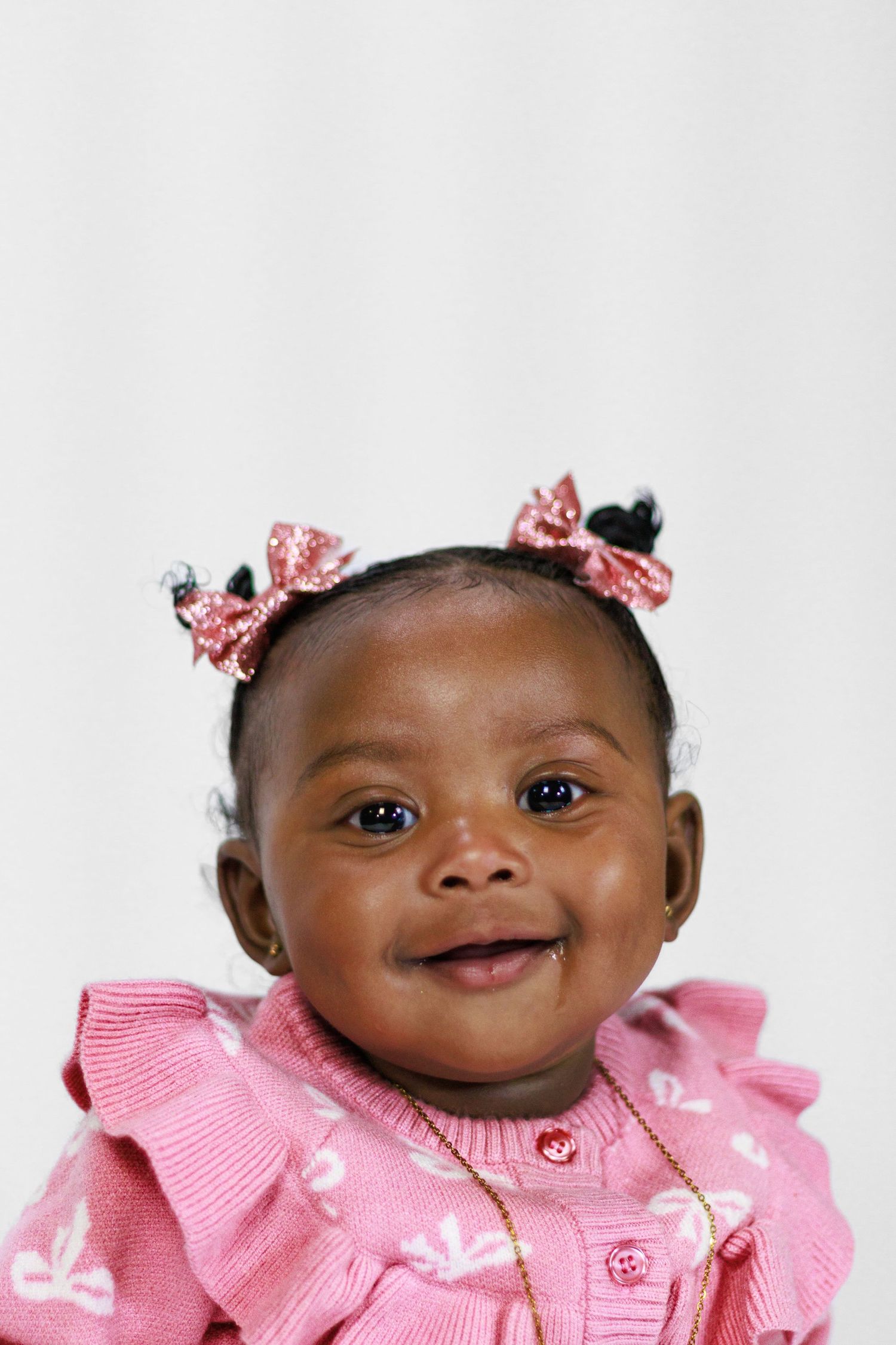 Adorable smiling baby girl in pink outfit with decorative bows in her hair.