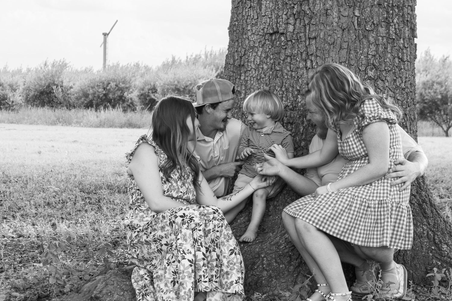 Black and white photo of a family with young children gathered around a tree trunk outdoors.