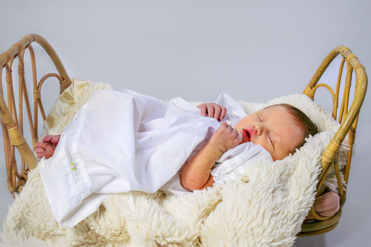Sleeping newborn baby wrapped in white blanket lying in a wicker bassinet.