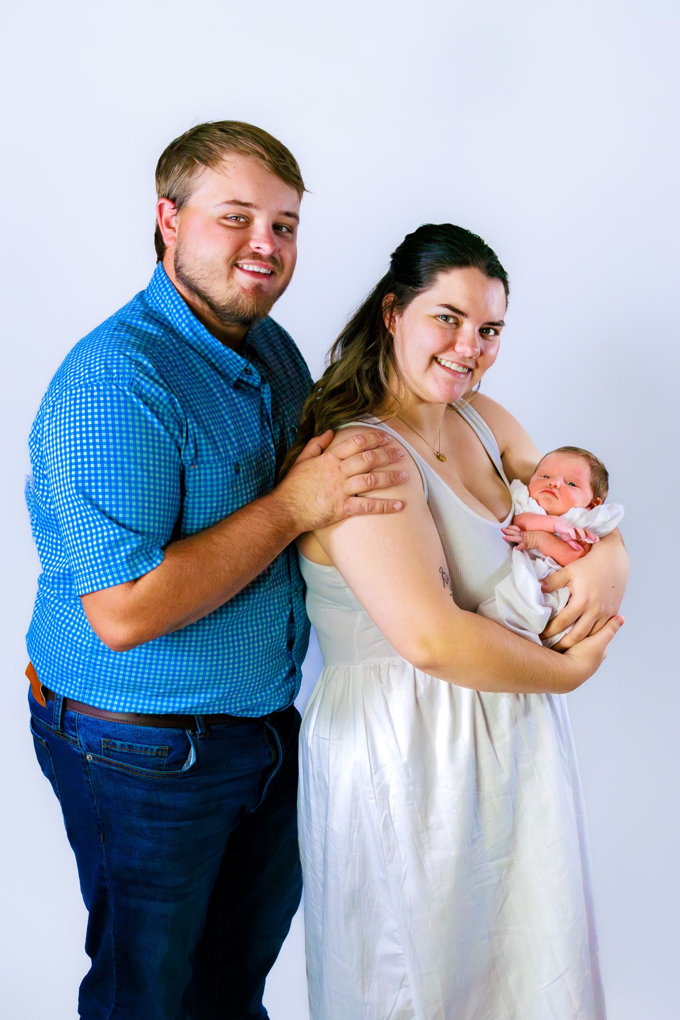 Smiling couple in white studio holding their newborn baby together.
