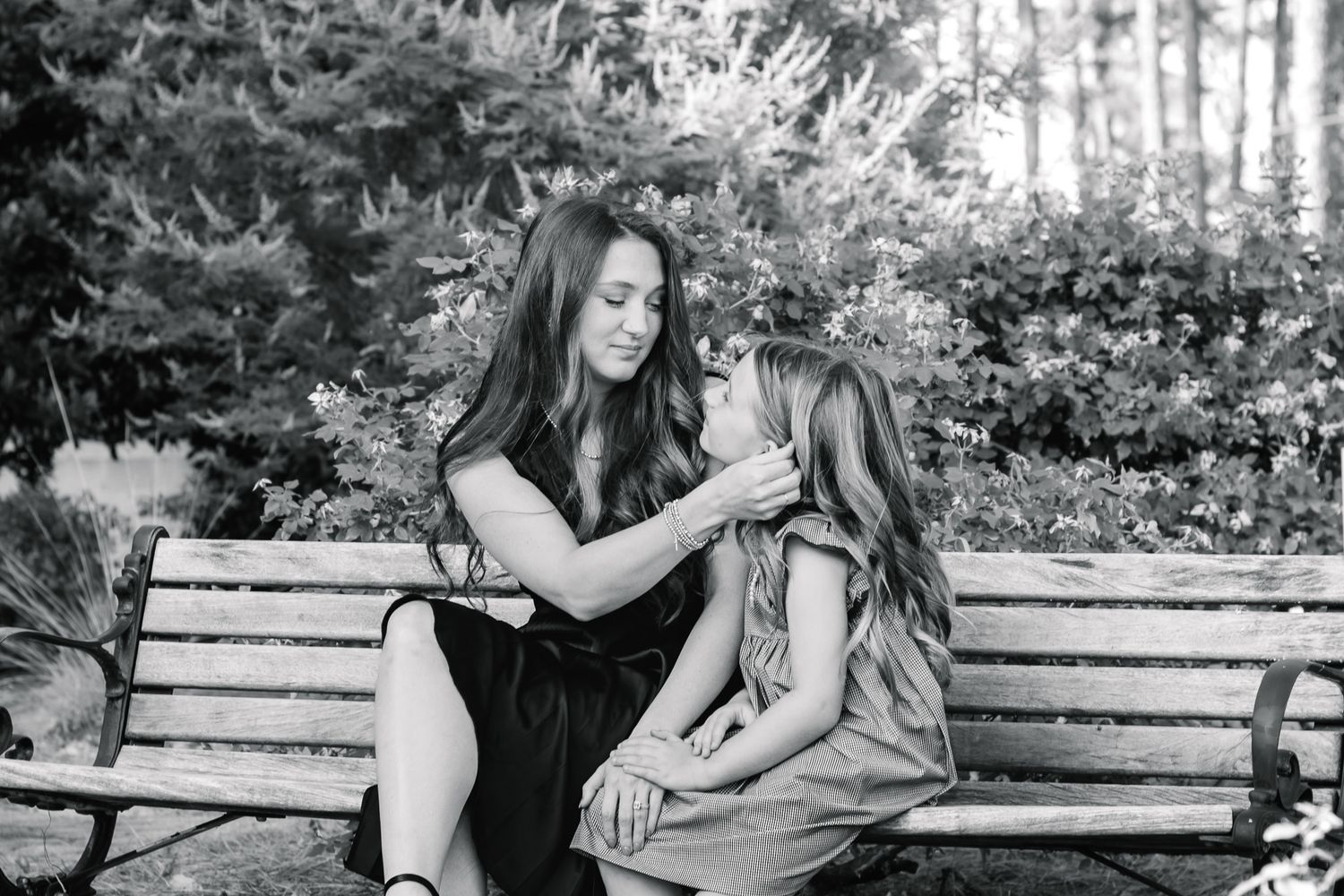 Woman tenderly touches young girl's face while sitting together on a park bench in black and white photo.
