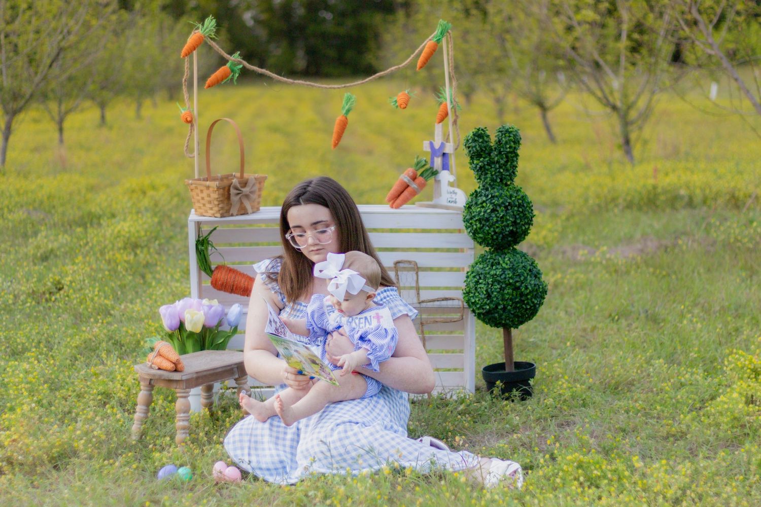 Mother and baby in matching blue dresses sit in field with Easter decorations.