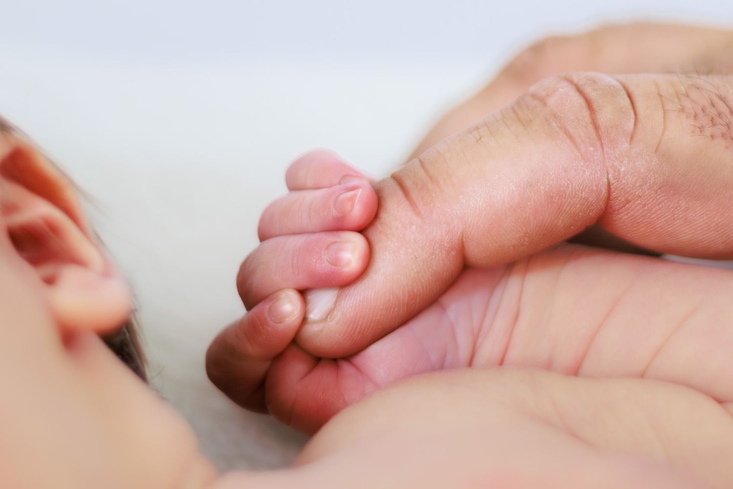 Close-up of a newborn baby's tiny hand grasping an adult's finger.