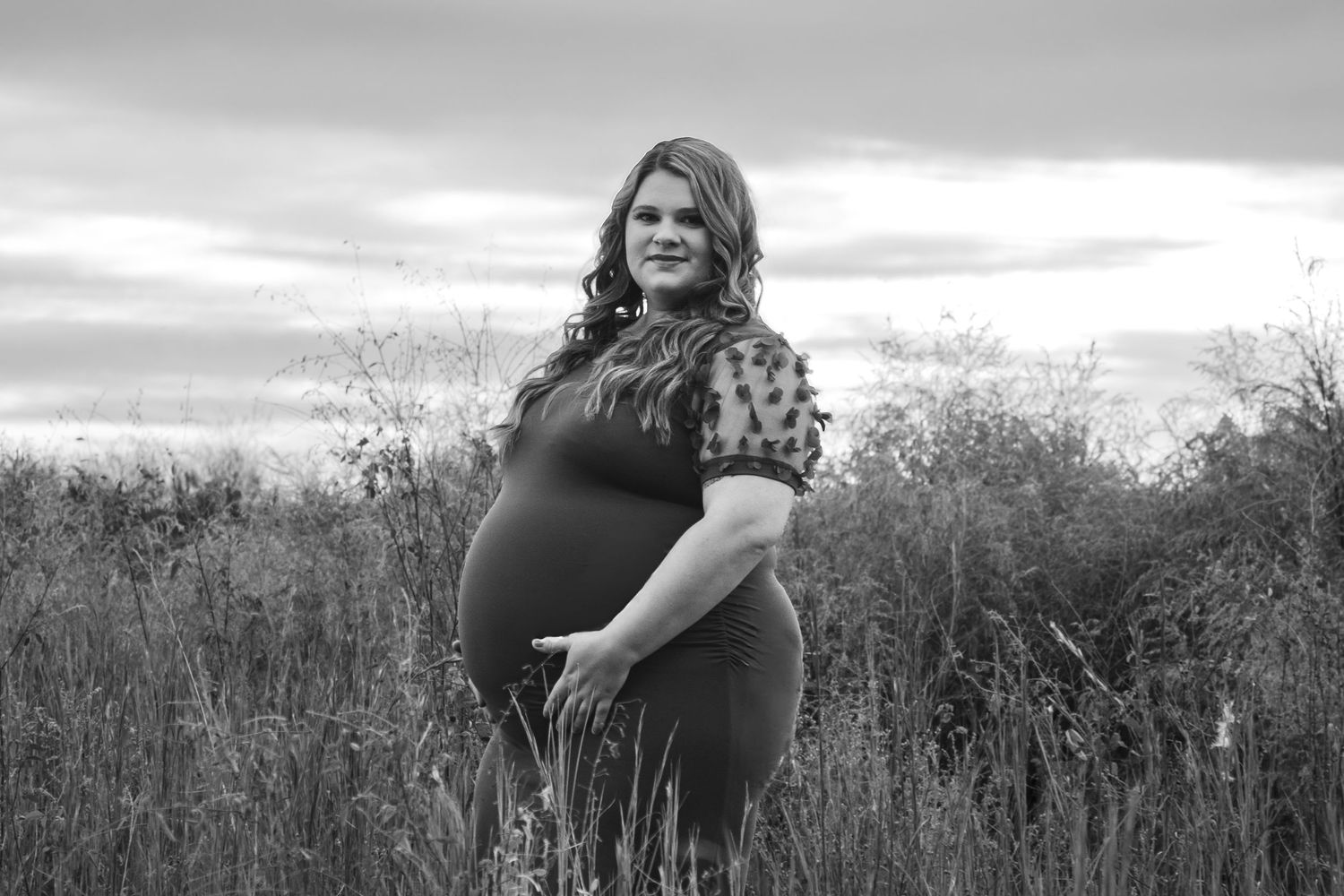 Black and white maternity photo of pregnant woman in field at dusk.